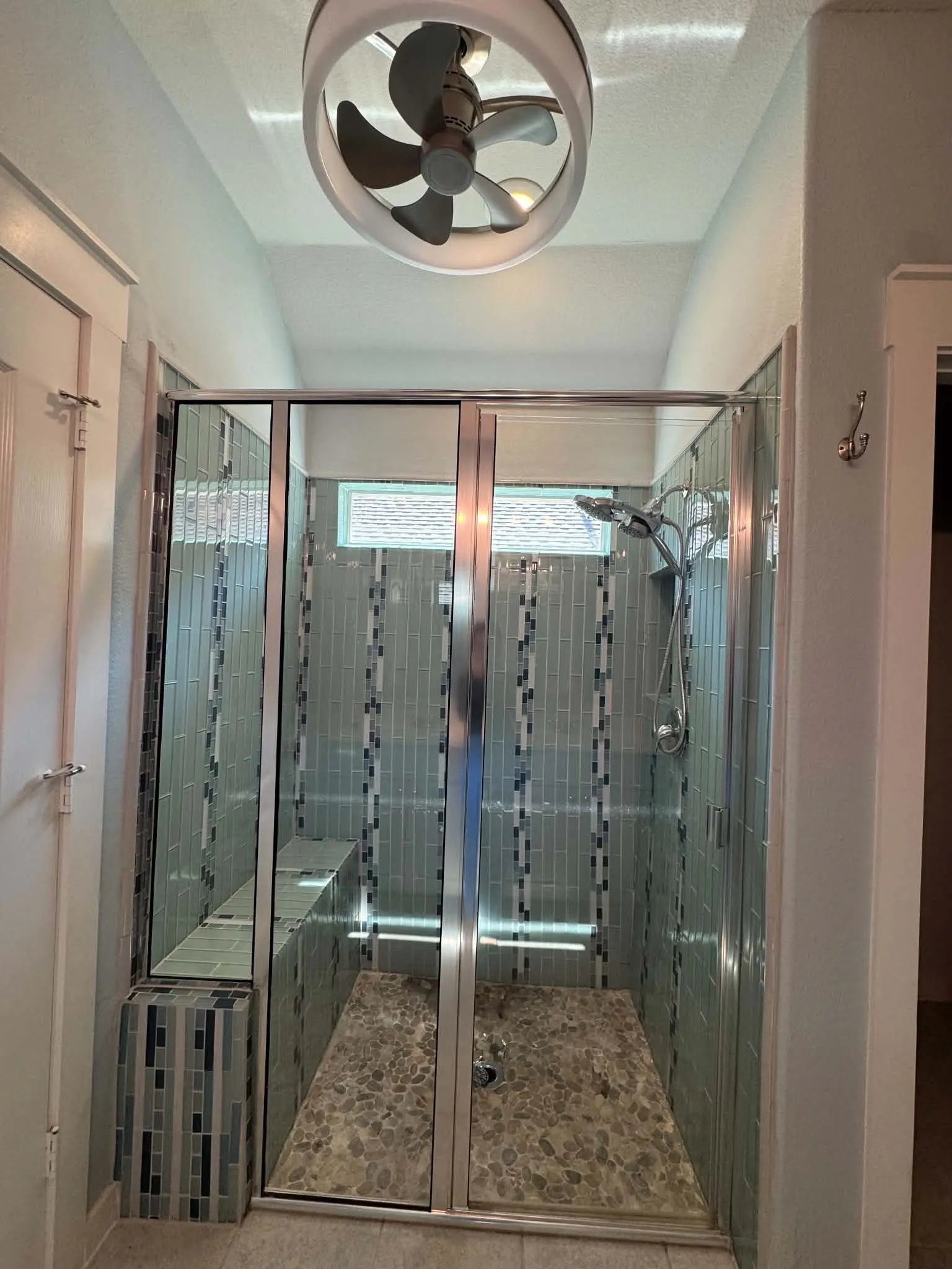 Glass-enclosed shower with pebble-finish flooring, tiled walls, a built-in bench, and a transom window