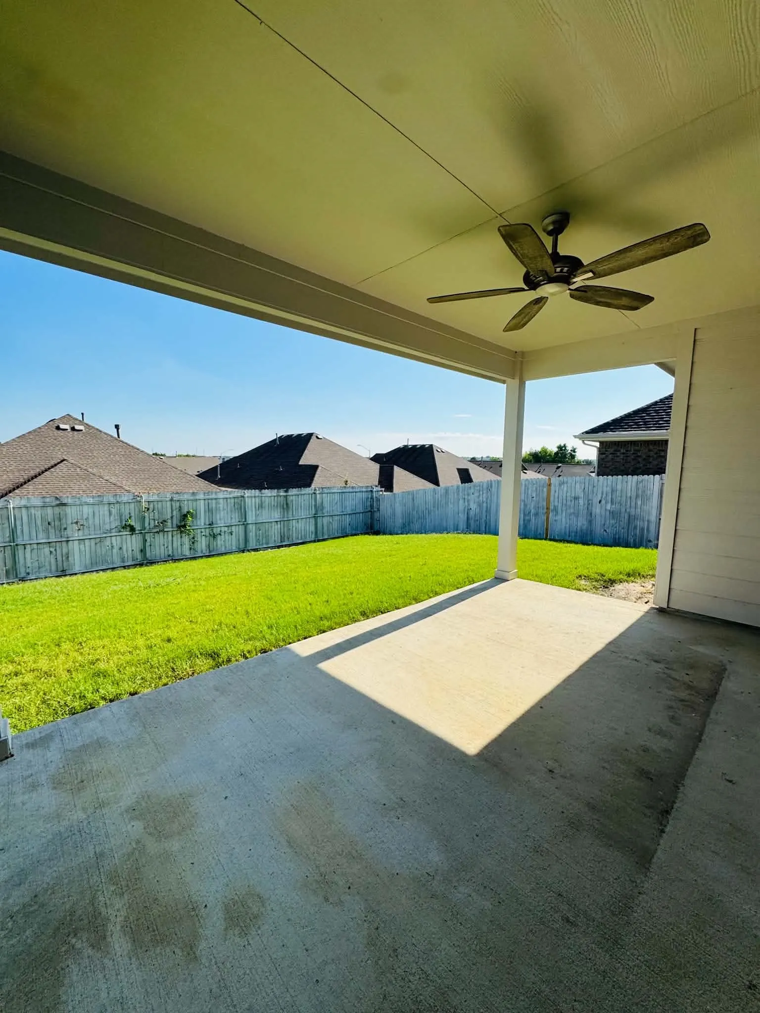 Covered patio featuring a ceiling fan, concrete flooring, and an expansive lawn