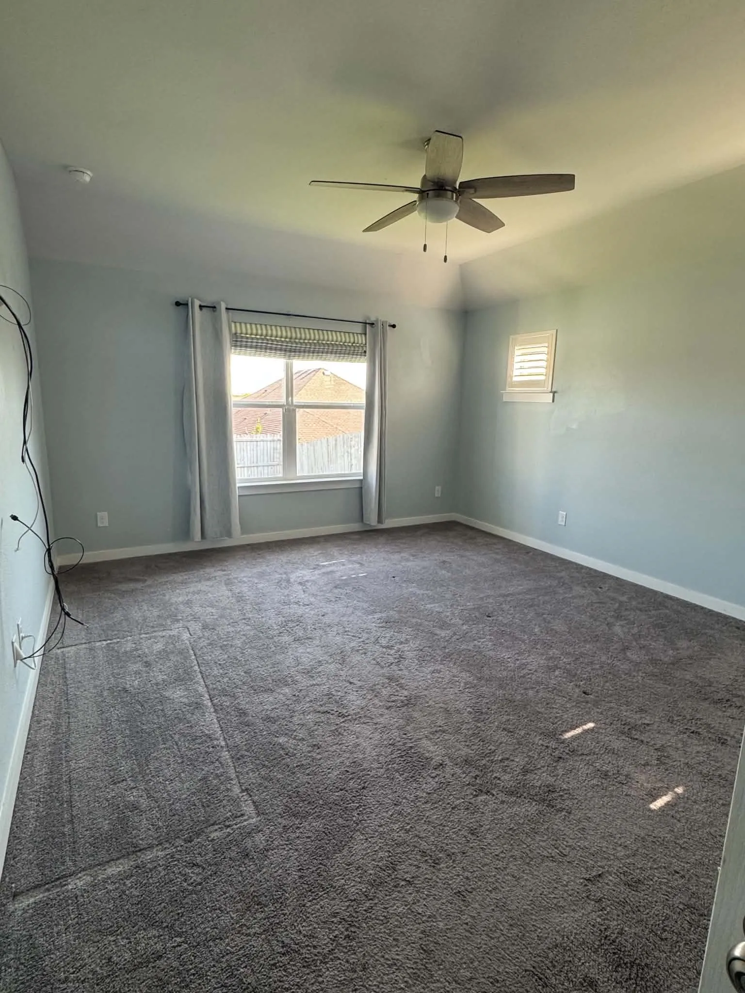 Spacious room featuring gray carpet, a ceiling fan with light fixture, and light blue wall paint