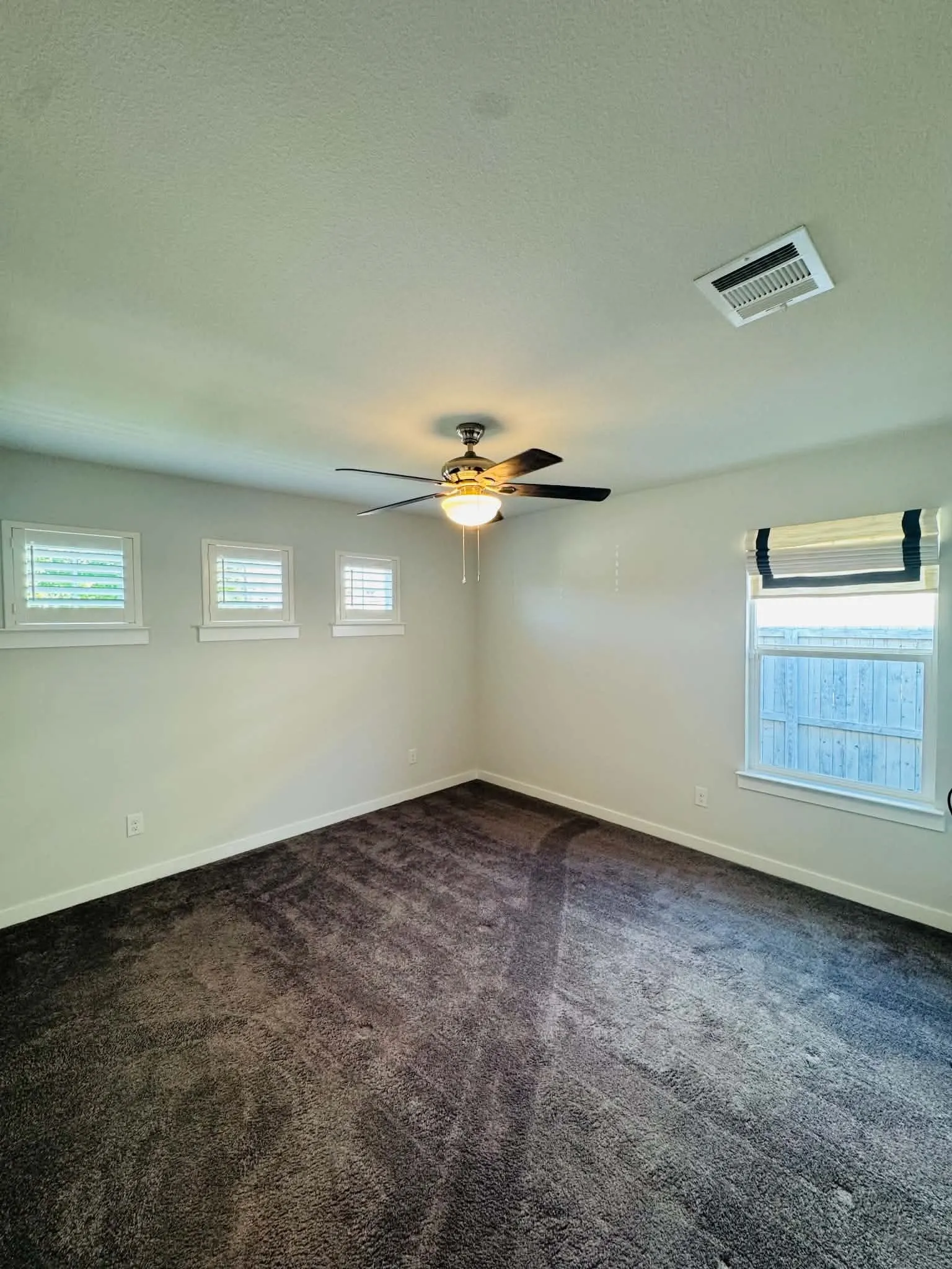 Plush grey carpeting and neutral wall tones define this room, featuring a ceiling fan with integrated lighting