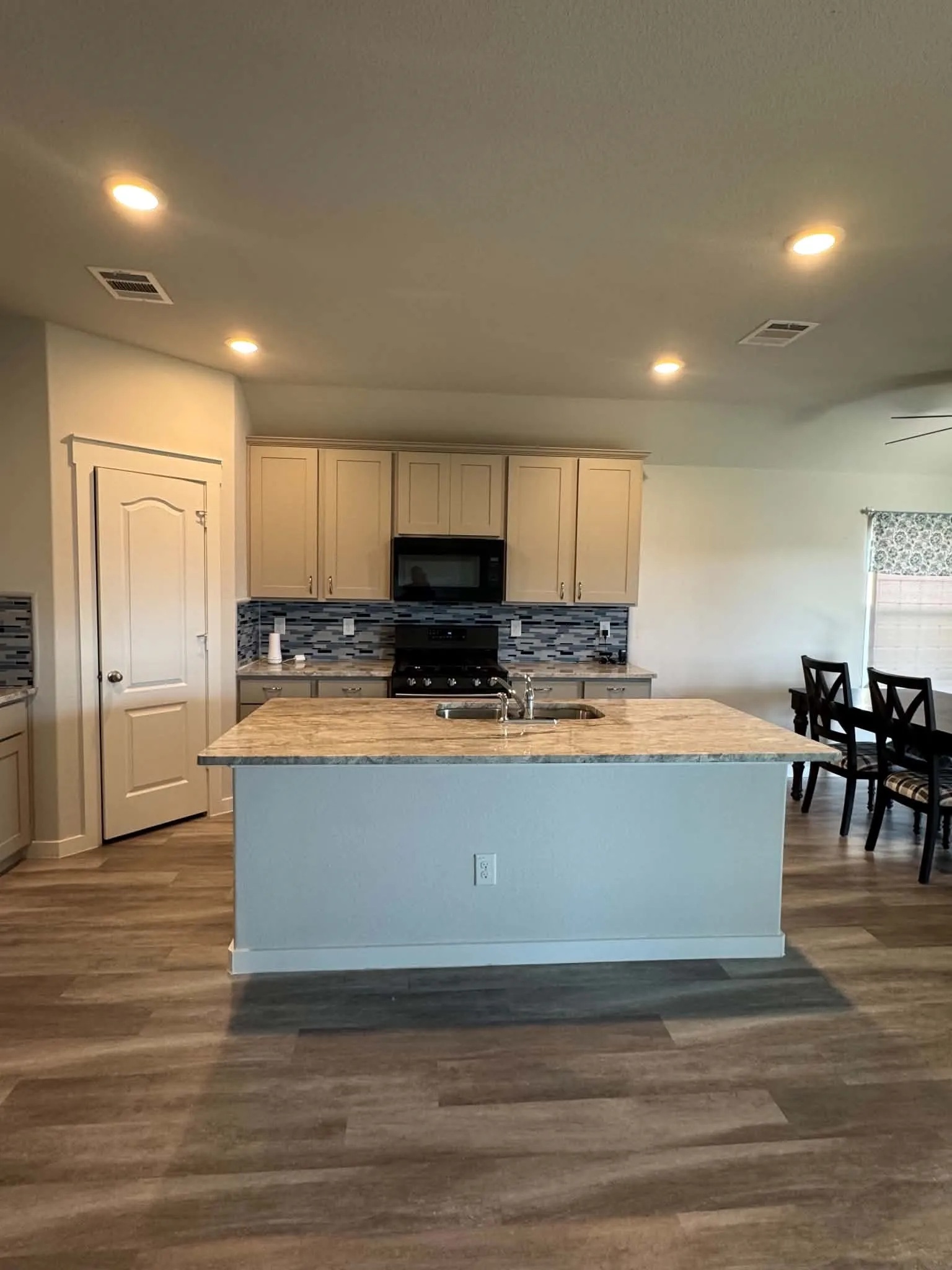 Open-concept kitchen featuring an island with an undermount sink, overhead recessed lighting, wood-finish flooring, a patterned tile backsplash, and light-toned cabinetry