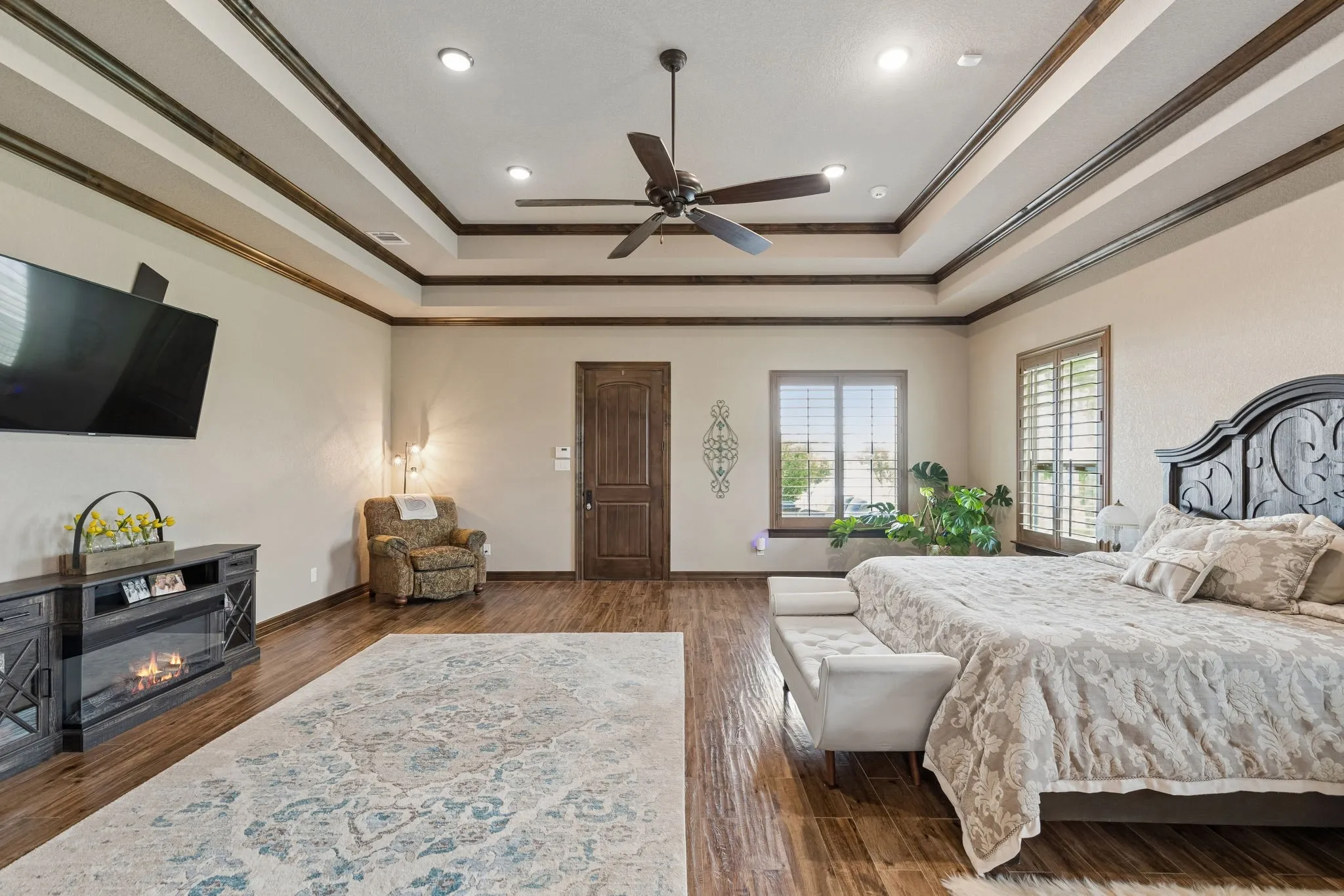 Spacious primary suite with a tray ceiling, stained crown molding, sitting area, view of the lake and private entrance to the side patio which has an outdoor fireplace, television and connections for a hot tub.