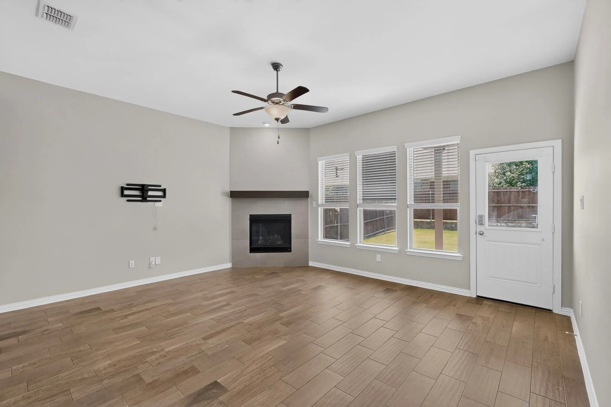Spacious room featuring wood-finish tile flooring, a corner fireplace with a dark wood mantle, and a ceiling fan