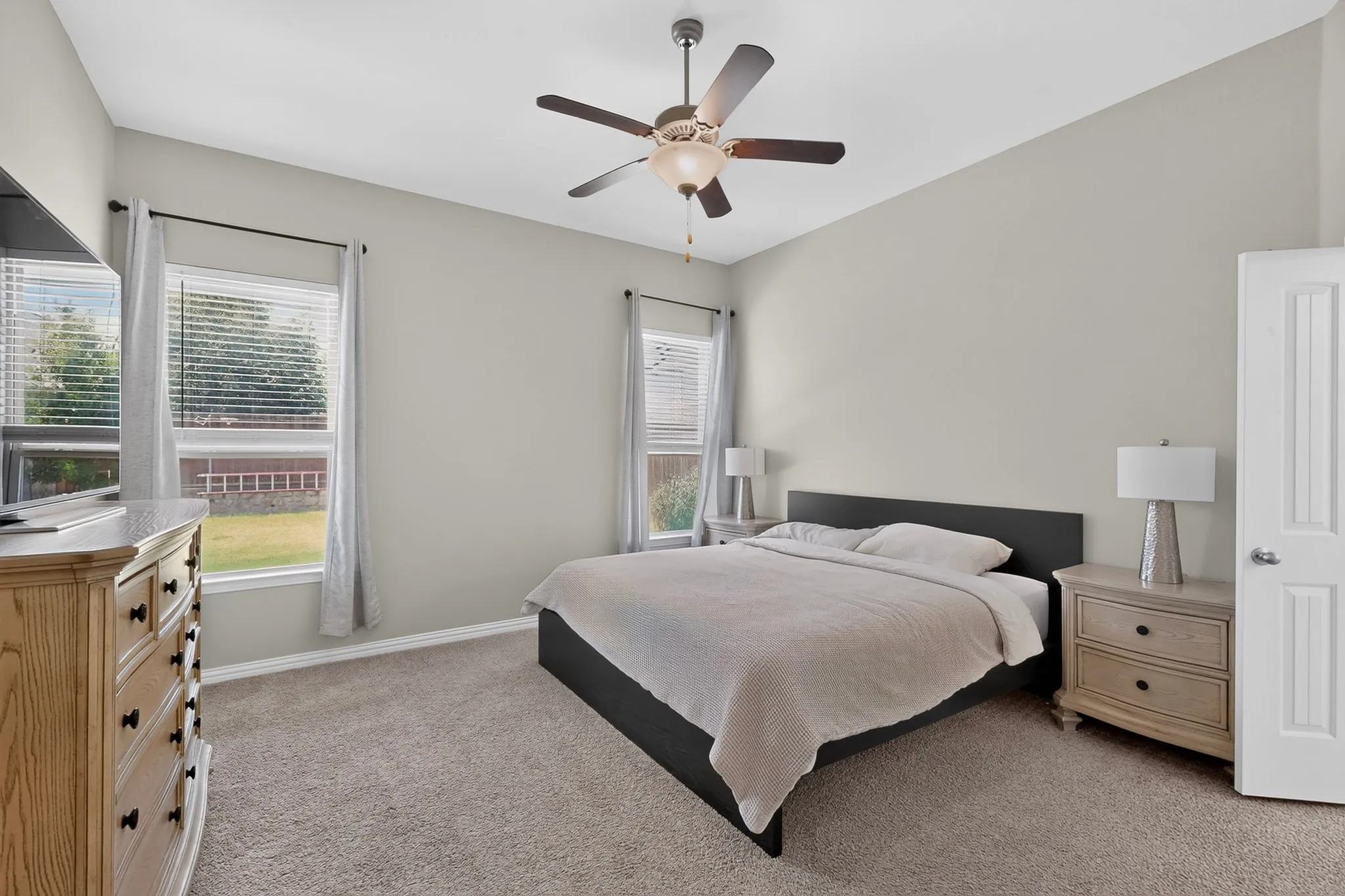 Carpeted bedroom featuring a ceiling fan with integrated lighting, two windows with blinds, and light gray wall paint