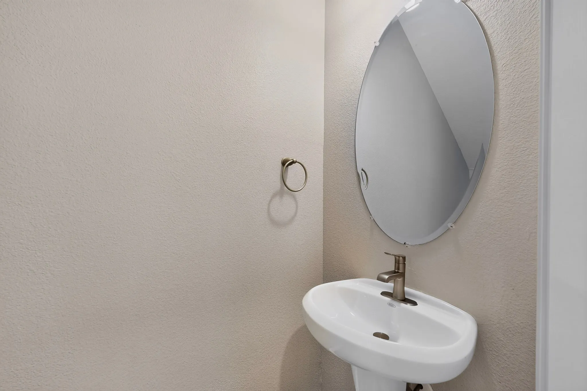 Pedestal sink with a brushed nickel faucet, an oval frameless mirror, and a coordinating towel ring