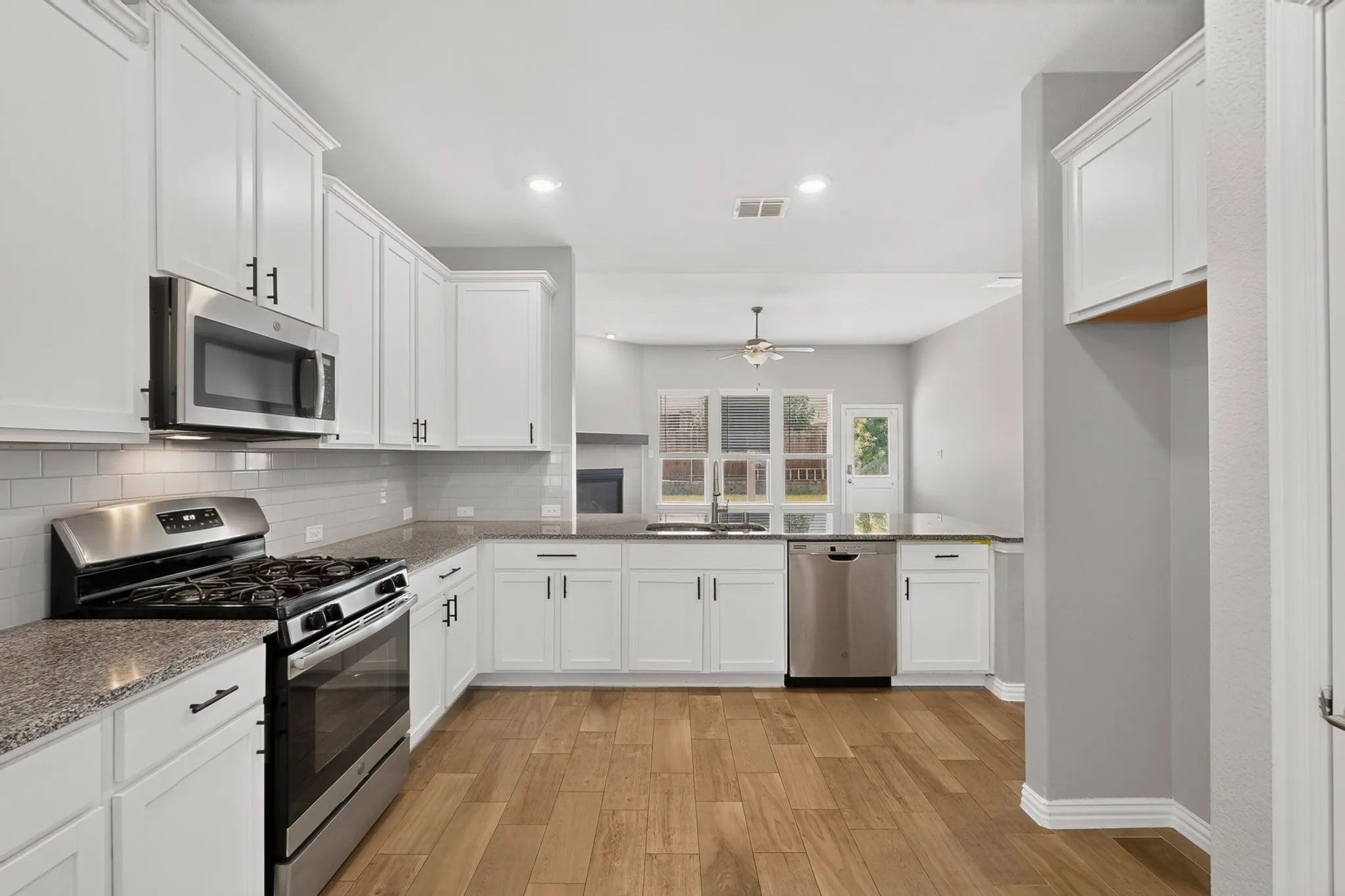 Kitchen featuring white cabinetry, stainless steel appliances, granite countertops, subway tile backsplash, and wood-finish flooring