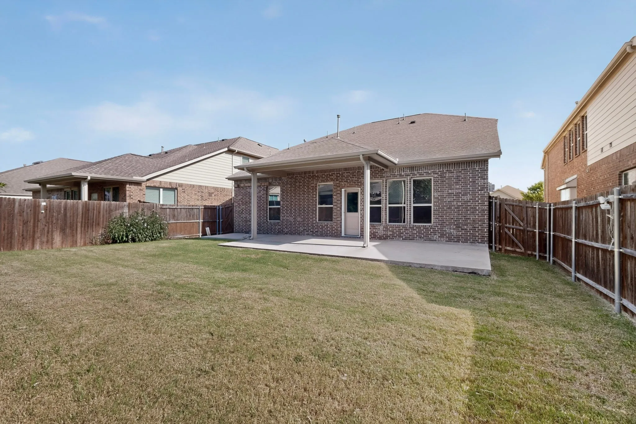 Expansive backyard with a covered concrete patio and a wooden privacy fence