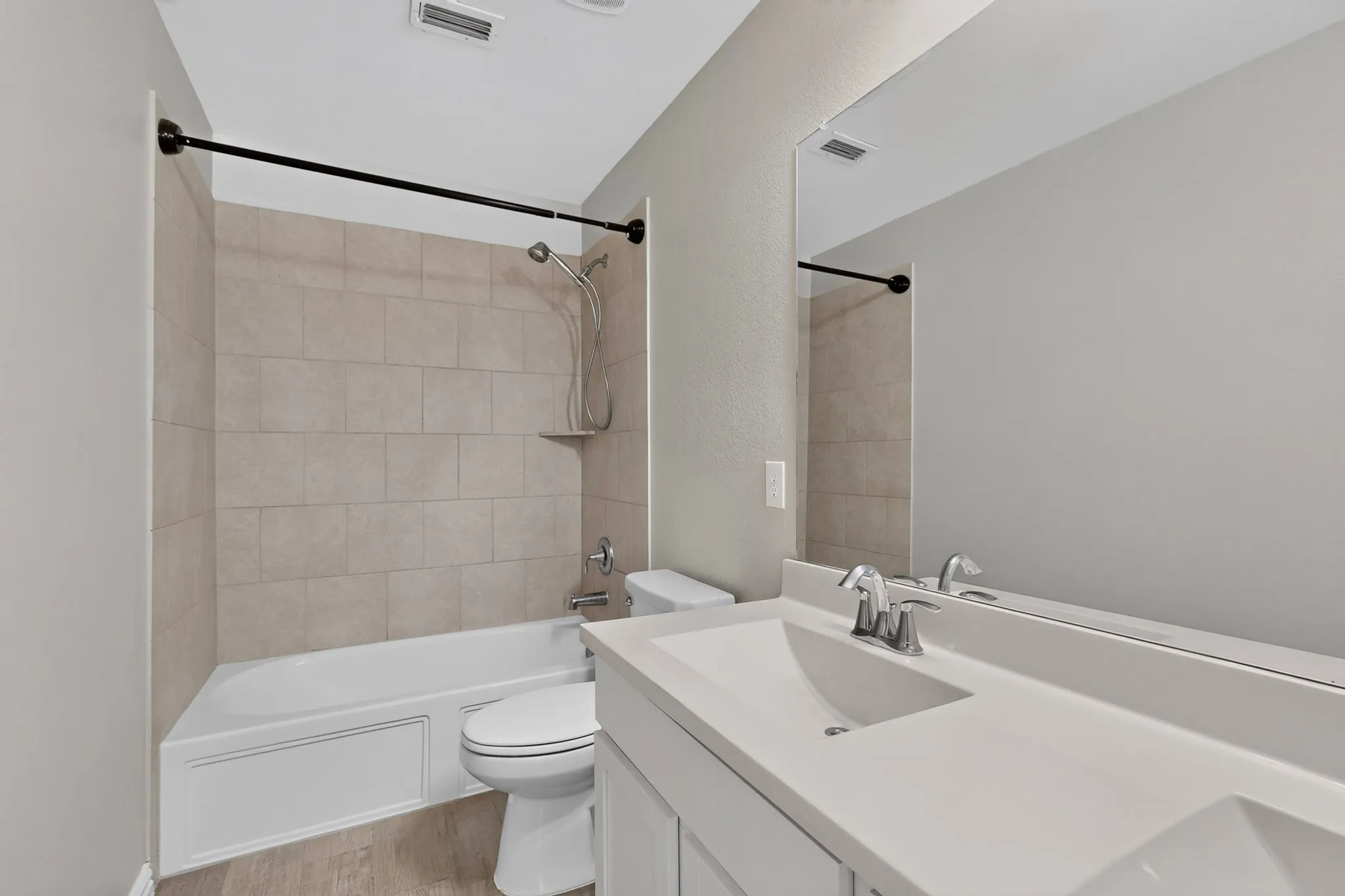 Full bathroom featuring a single vanity with a white countertop and integrated sink, a large wall-mounted mirror, a toilet, and a bathtub with a tiled surround