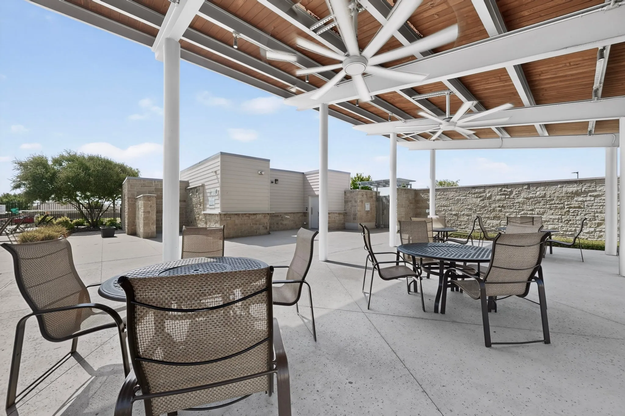Covered outdoor patio featuring a wood-panel ceiling with two large ceiling fans, supported by white columns