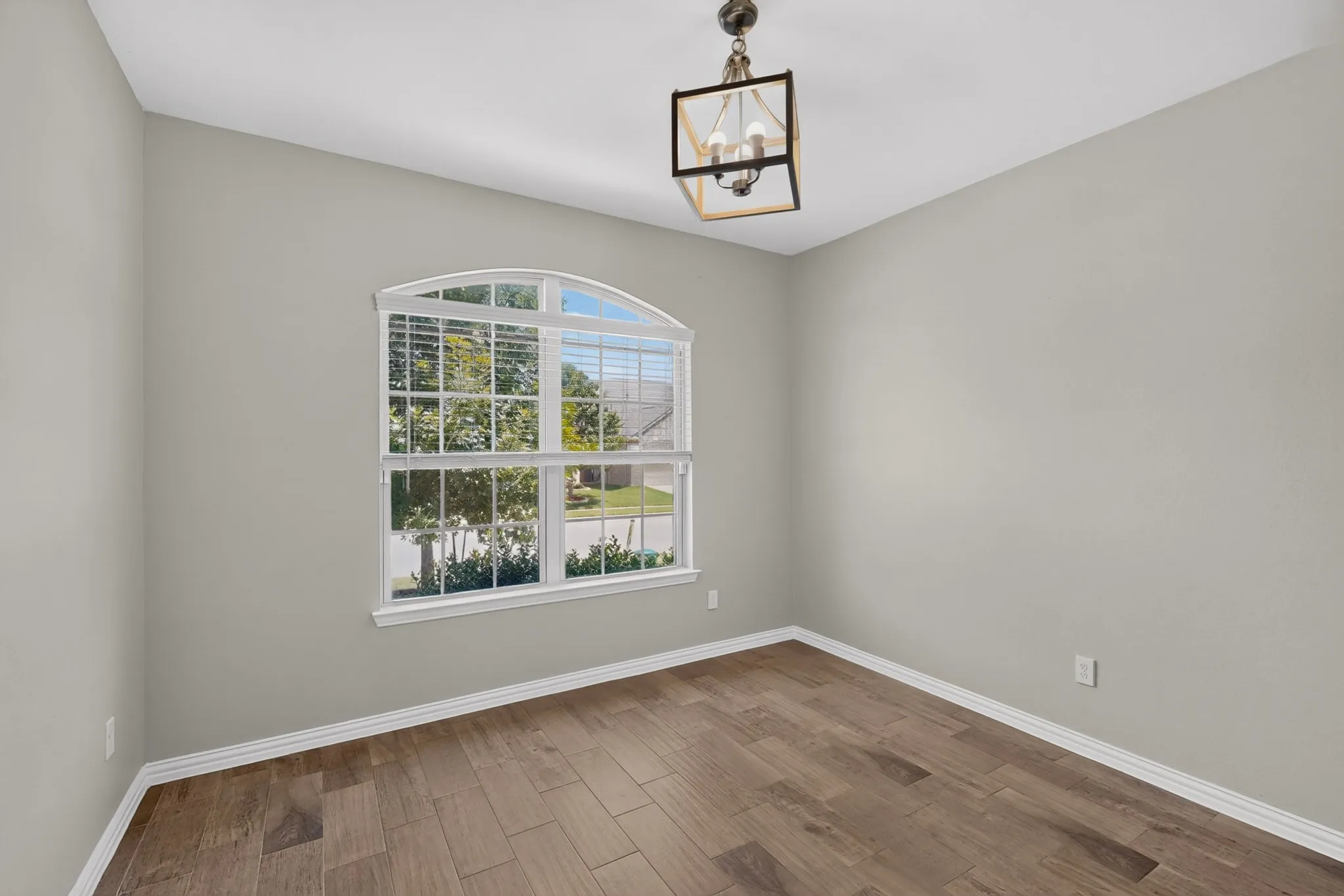Room featuring an arched window, wood-finish flooring, and a decorative ceiling fixture