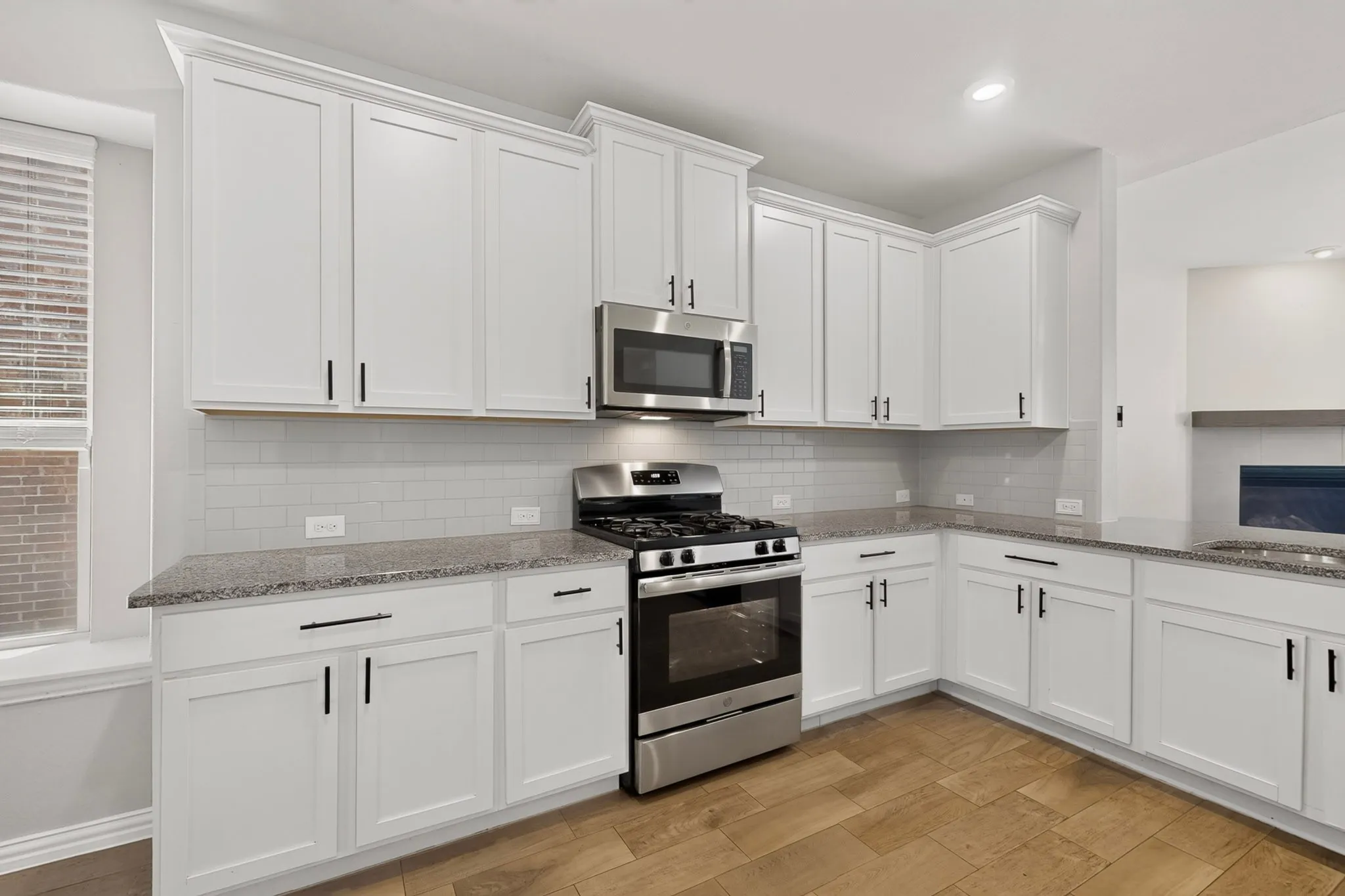 Contemporary kitchen featuring white shaker cabinetry, stainless steel appliances, granite countertops, subway tile backsplash, and wood-finish flooring