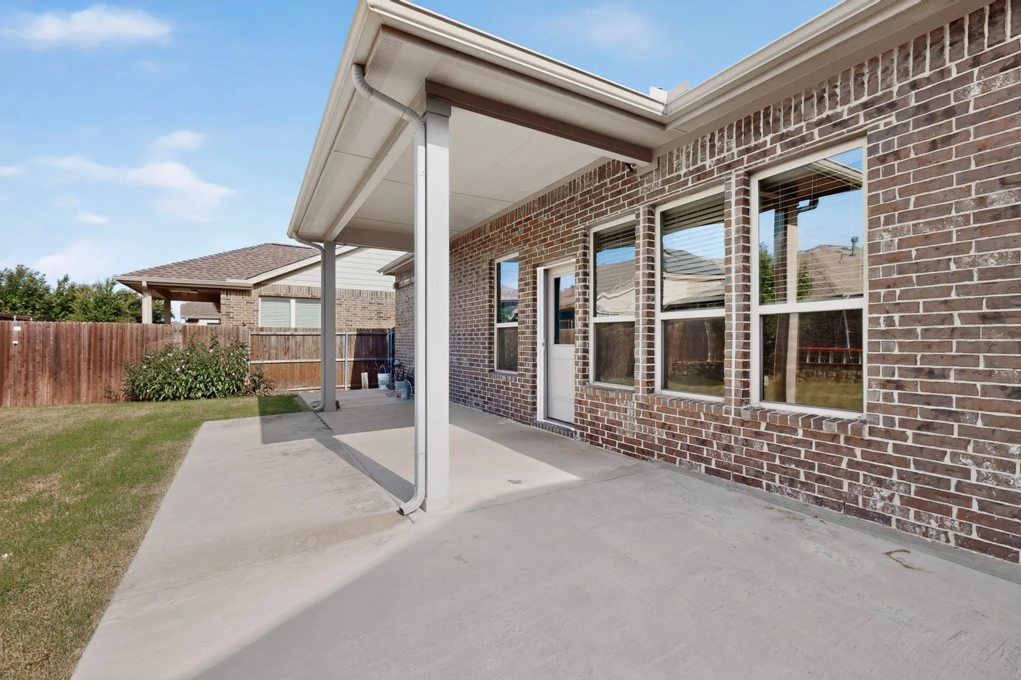 Covered patio area featuring a concrete surface, brick exterior, multiple windows with blinds, and white trim