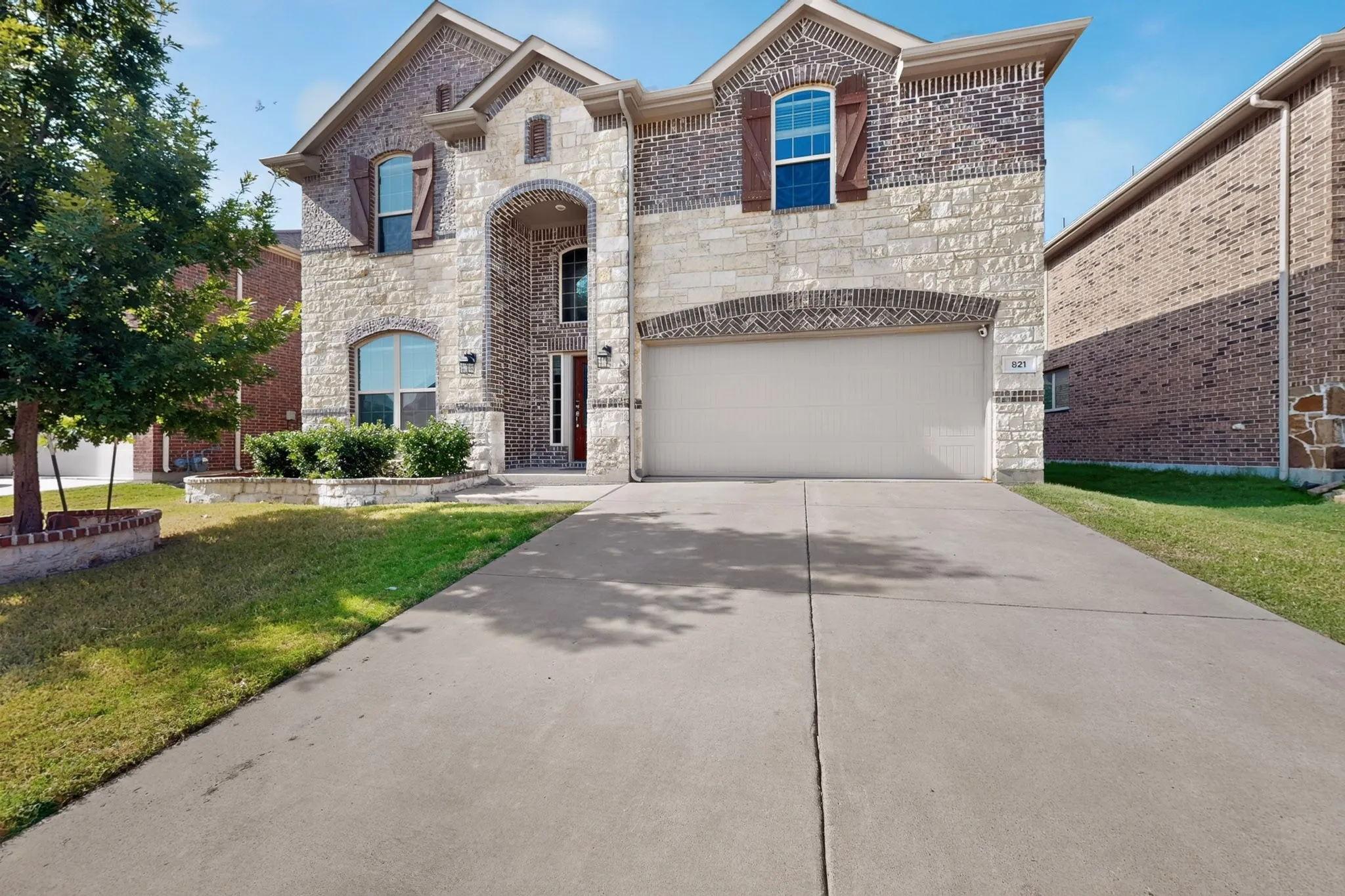 Two-story residence featuring a stone and brick facade, a two-car garage, and a concrete driveway