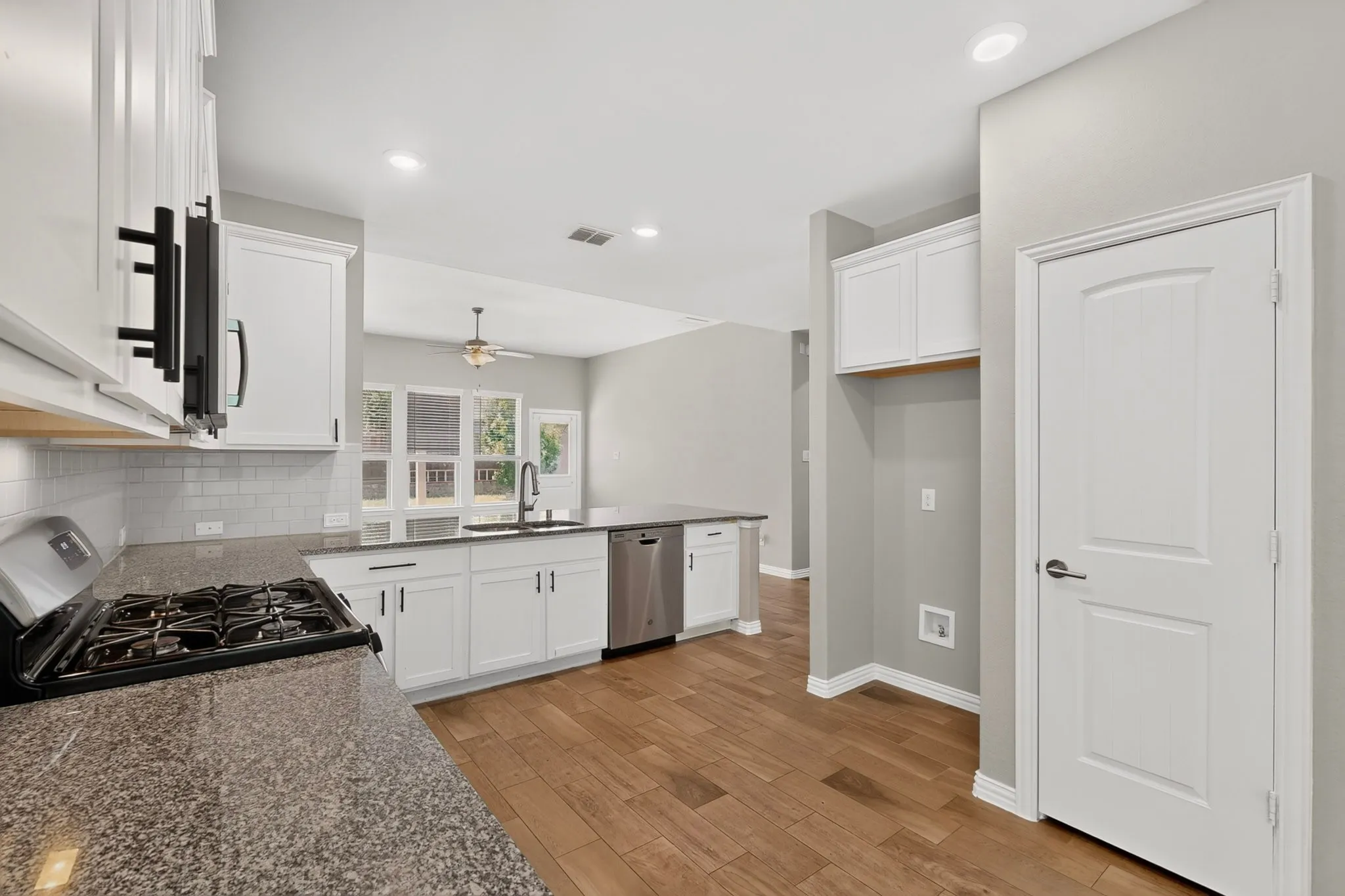 Kitchen featuring white cabinetry, granite countertops, stainless steel gas range, wood-finish flooring, and a subway tile backsplash