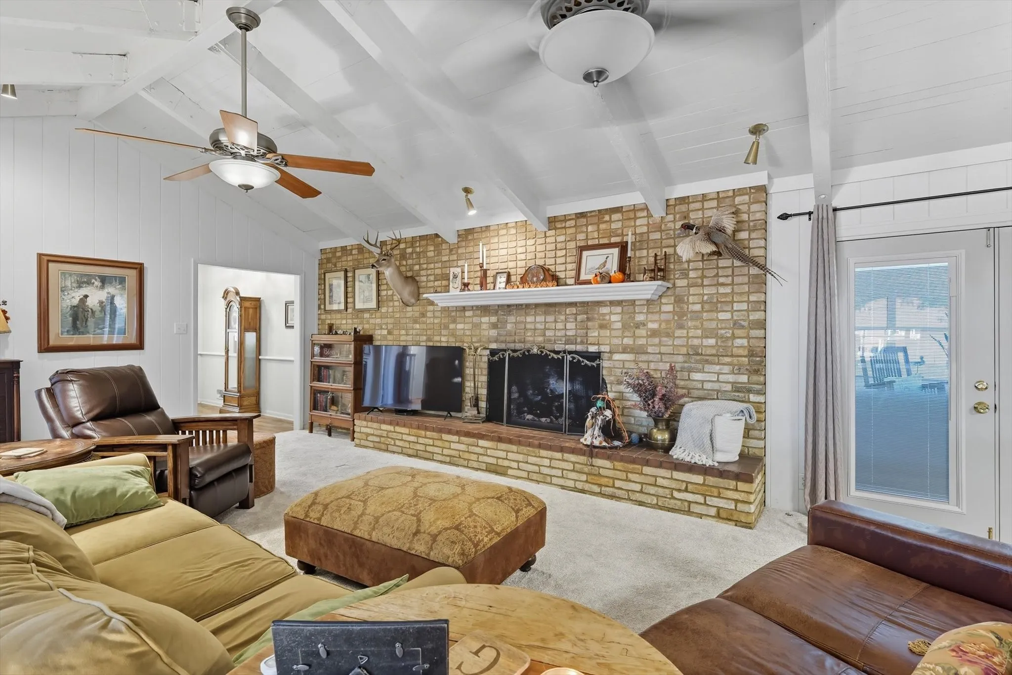 Carpeted living area featuring a brick fireplace, a ceiling fan, and brick wall