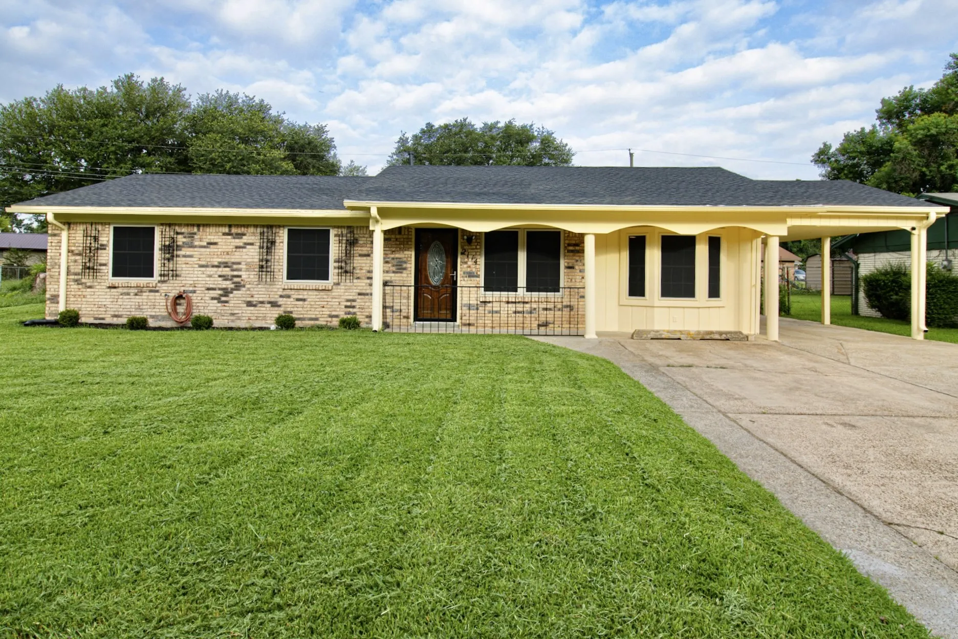 Brick exterior residence featuring a dark shingle roof, a covered carport, and an arched entry porch with decorative railings