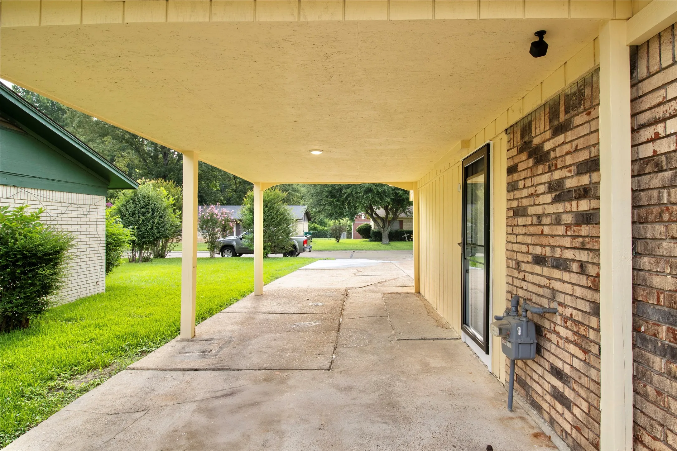 Covered carport with concrete paving, brick facade, and a side entry door