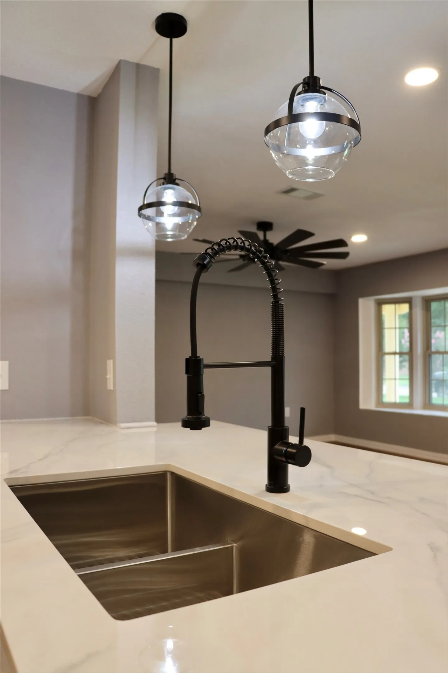 Kitchen island featuring a double-basin stainless steel sink, a matte black gooseneck faucet, and a light-toned countertop with subtle veining