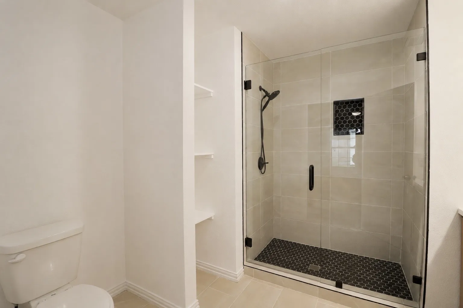 Walk-in shower featuring a frameless glass enclosure, dark hexagonal tile floor, and large format wall tiles