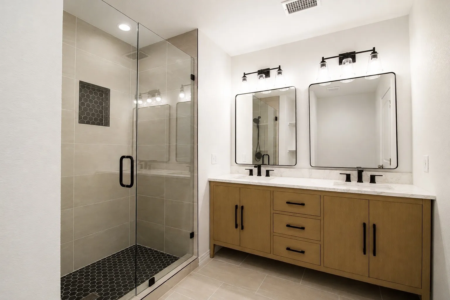 Bathroom featuring a glass-enclosed shower with honeycomb tile accent, dual vanity with solid surface countertop, and individual framed mirrors with integrated lighting