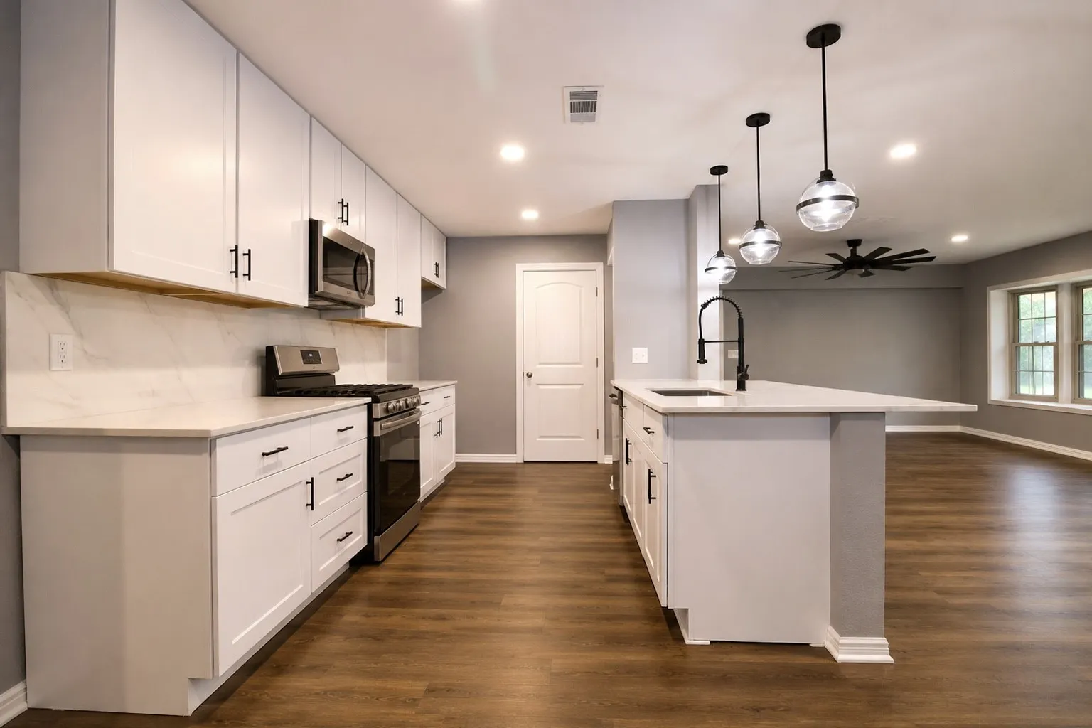 Modern kitchen featuring white cabinetry, light-toned countertops with a matching backsplash, stainless steel appliances, and a central island with a built-in sink and matte black faucet