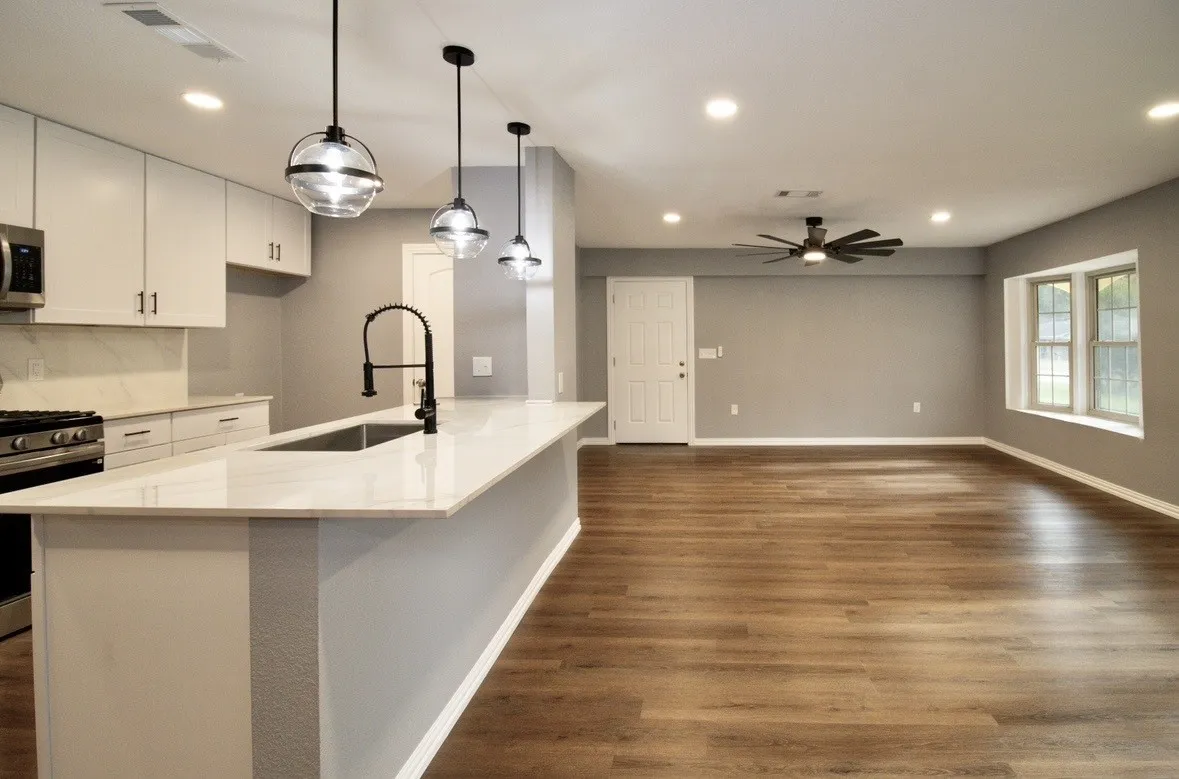 Open-concept kitchen and living area featuring a kitchen island with sink, white shaker cabinetry, stainless steel appliances, wood-finish flooring, and recessed lighting