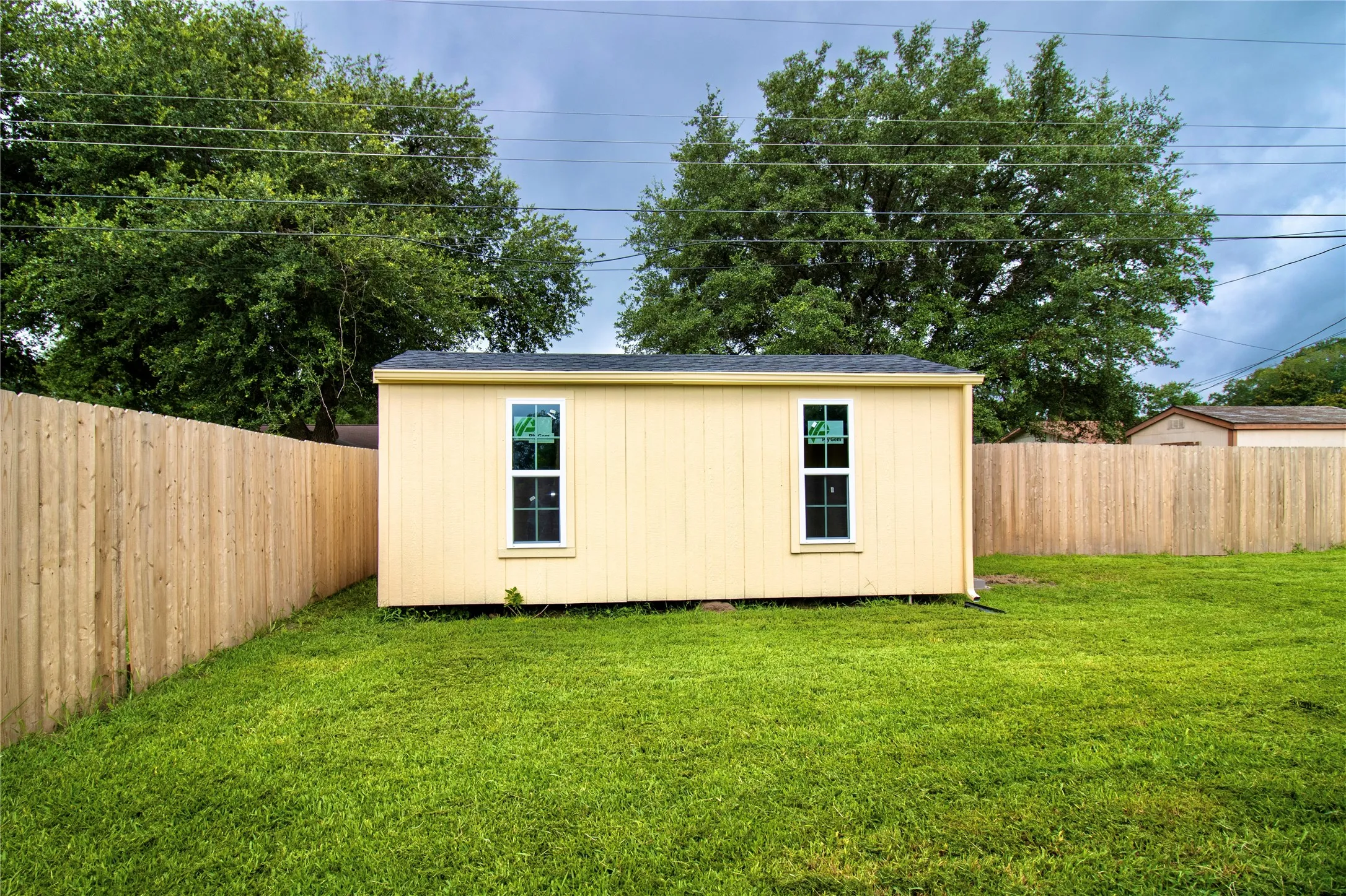 Detached auxiliary structure with vertical siding, two vertical windows, and a dark shingle roof