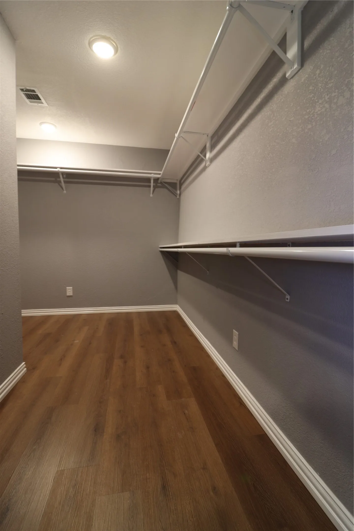 Spacious walk-in closet featuring wood-finish flooring, recessed lighting, and extensive white shelving with hanging rods