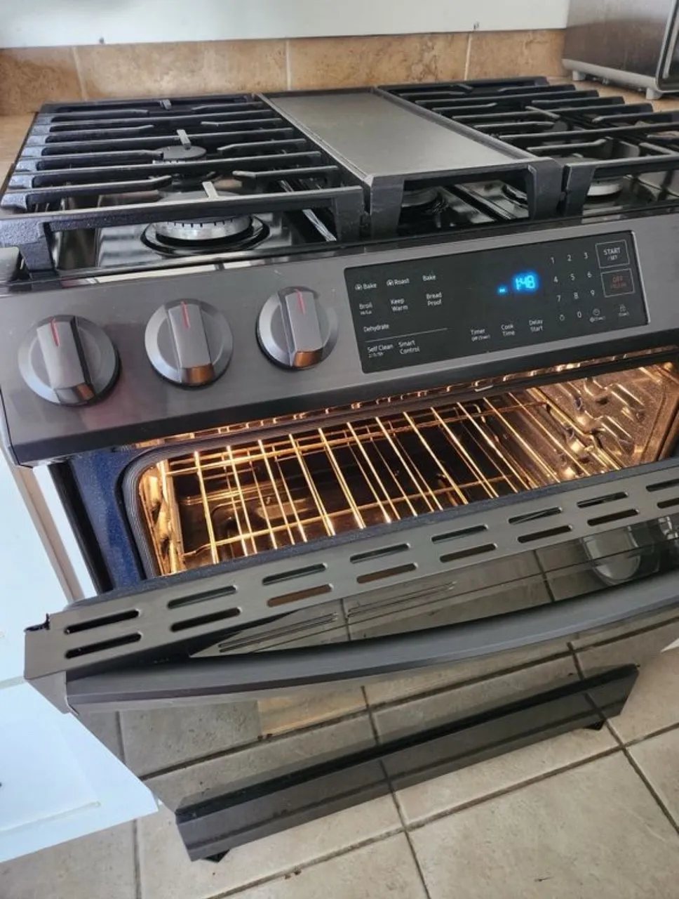 Stainless steel range with a gas cooktop, integrated griddle, digital display, and illuminated oven interior