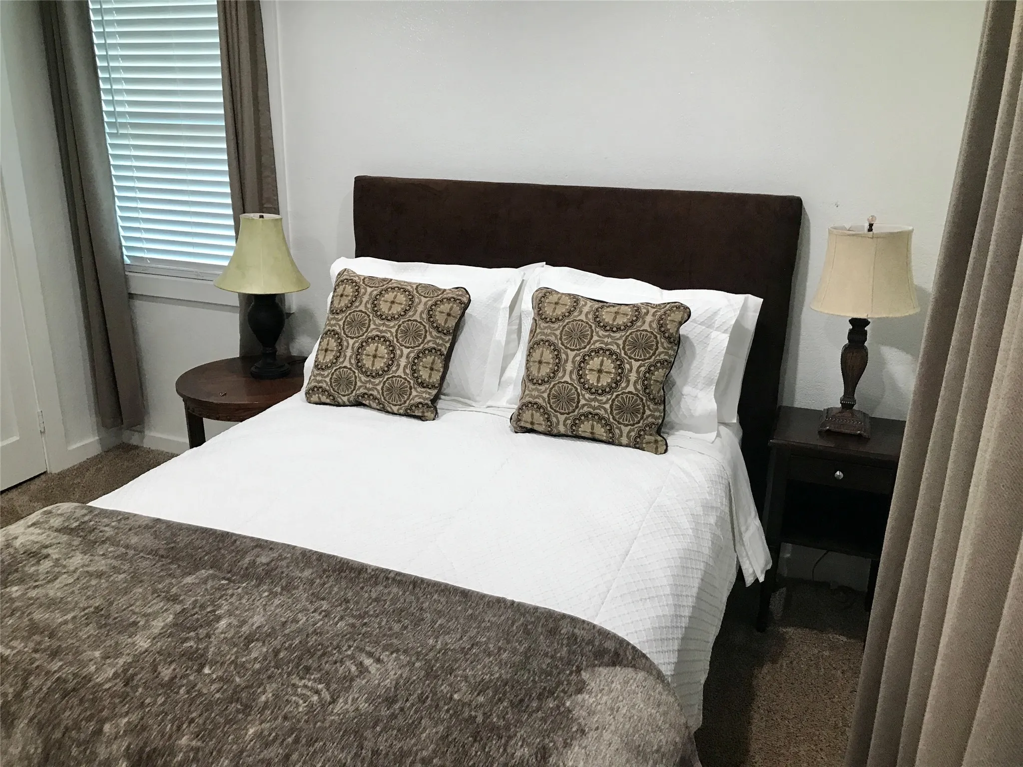Bedroom featuring neutral-toned carpet flooring, white walls, and a window with blinds and drapes