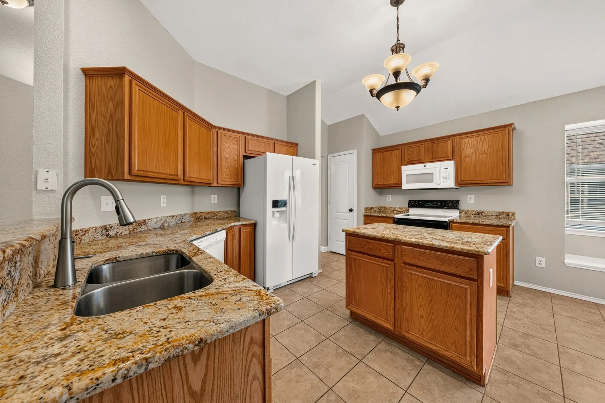 Kitchen featuring a dual basin sink with a pull-down faucet, granite countertops, wood cabinetry, and a central island
