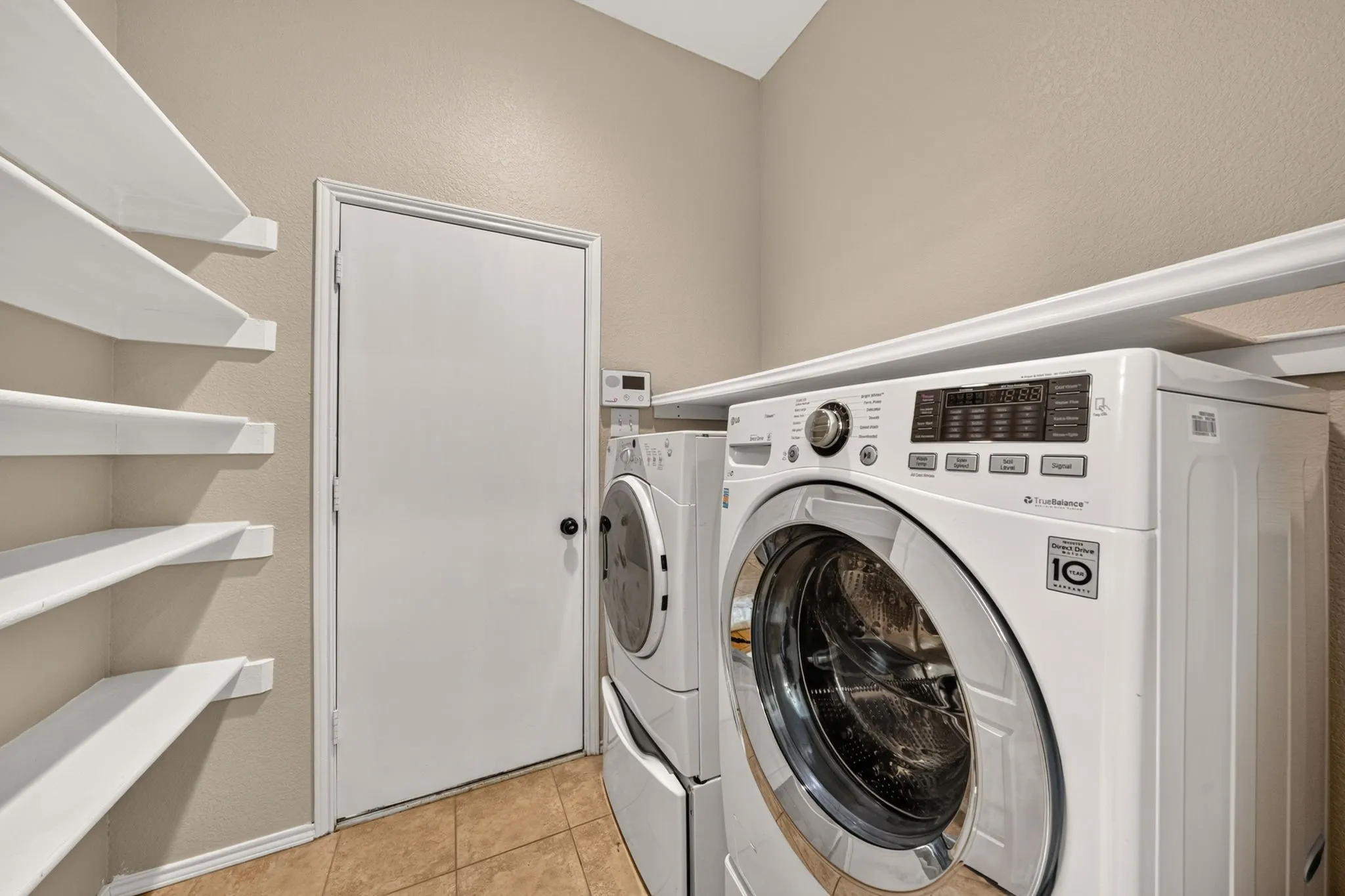 Dedicated laundry area featuring a tiled floor, built-in white shelving for extra pantry space, linens or cleaners etc. and neutral wall tones
