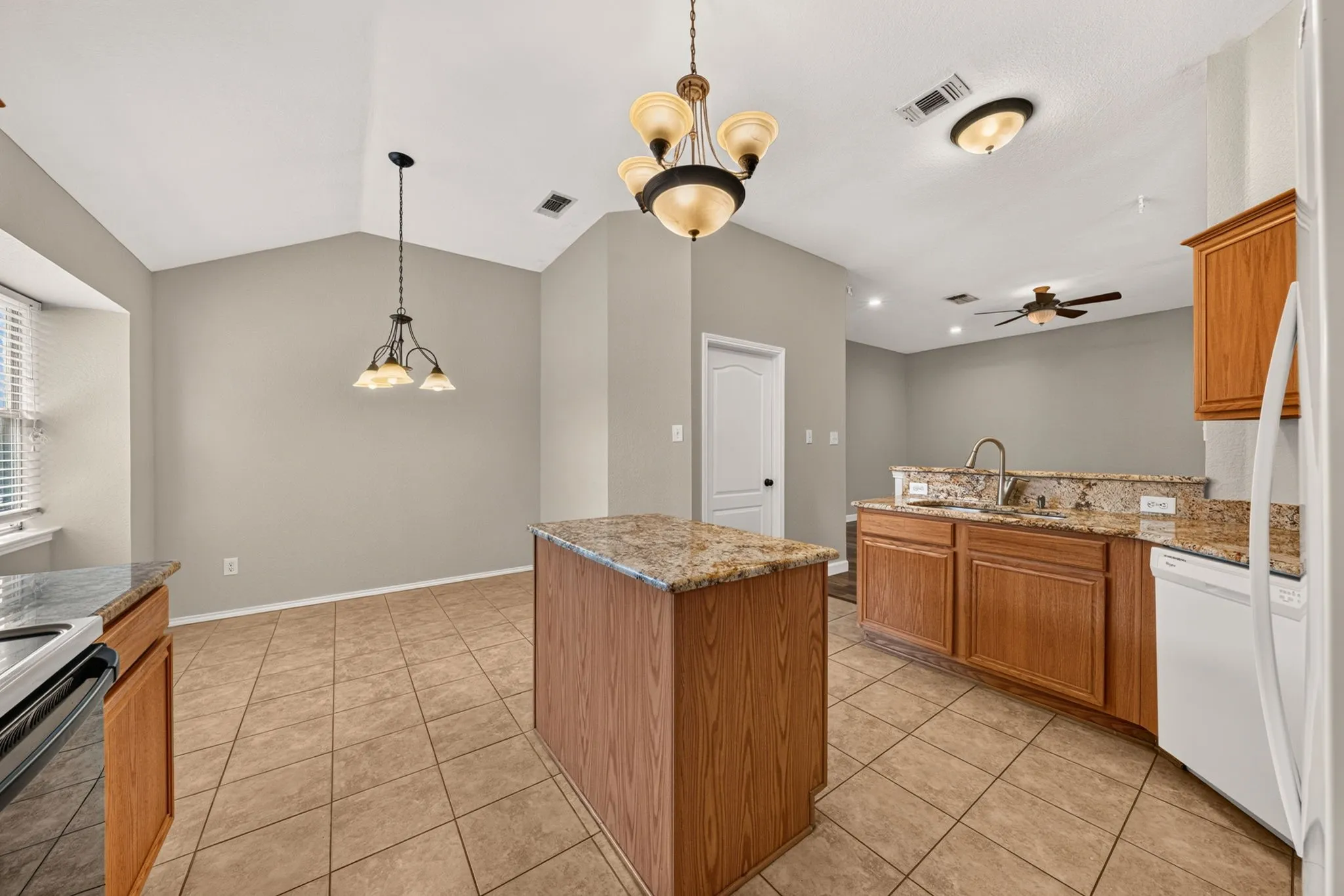 Kitchen featuring a central island with a stone-finish countertop, wood-finish cabinetry, tile flooring, an integrated sink with a high-arc faucet, and an adjacent dining area with vaulted ceilings