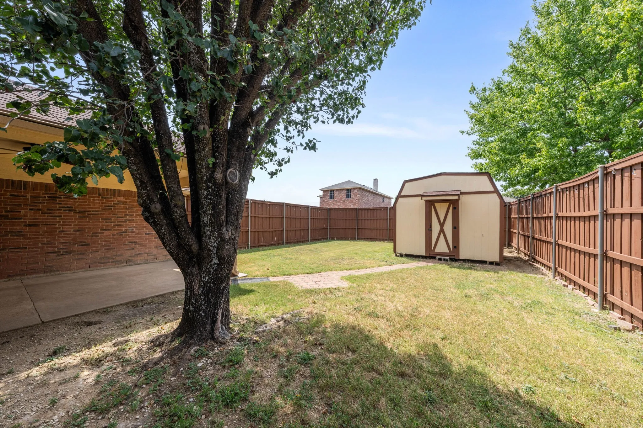Spacious backyard featuring a storage shed with a gambrel roof, full wood fencing, and a mature tree providing natural shade