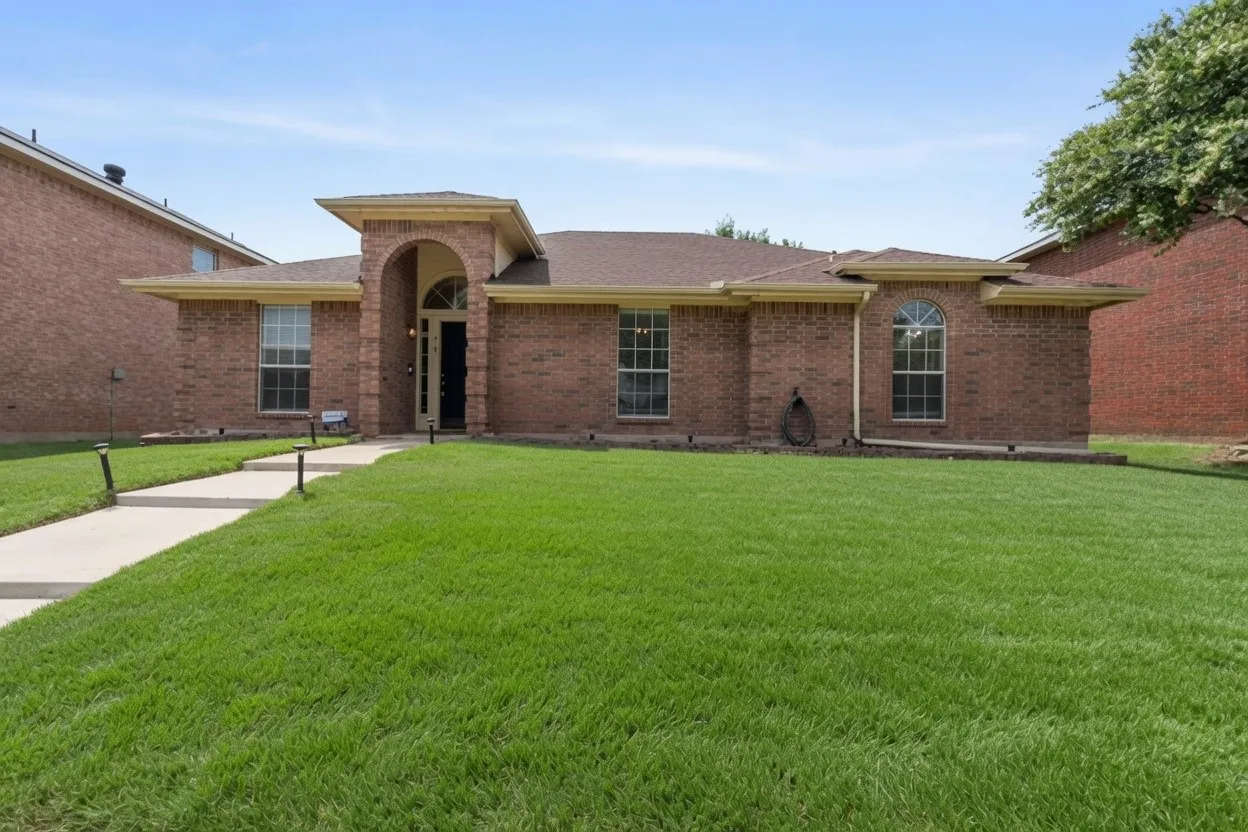 Brick Colonial residence showcasing a manicured lawn, concrete walkway with entry portico, arched entryway with stone accents, multi-pane windows, and mature landscaping framing the property perimeter