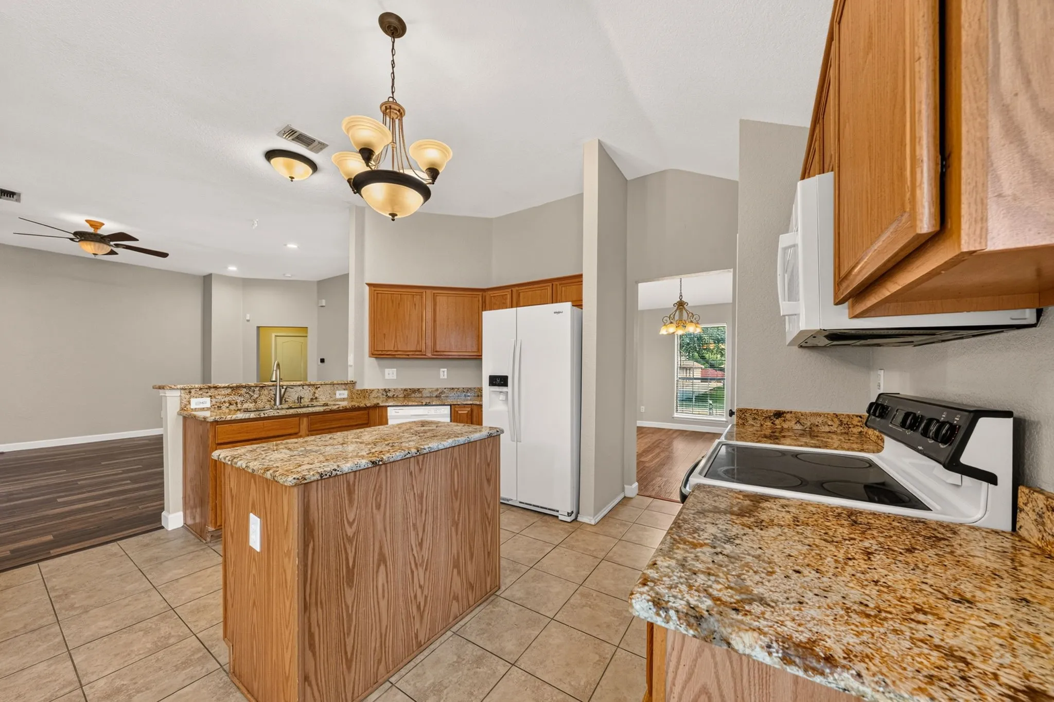 Kitchen featuring a central island, tan granite-finish countertops, natural wood cabinetry, white appliances, and tiled flooring