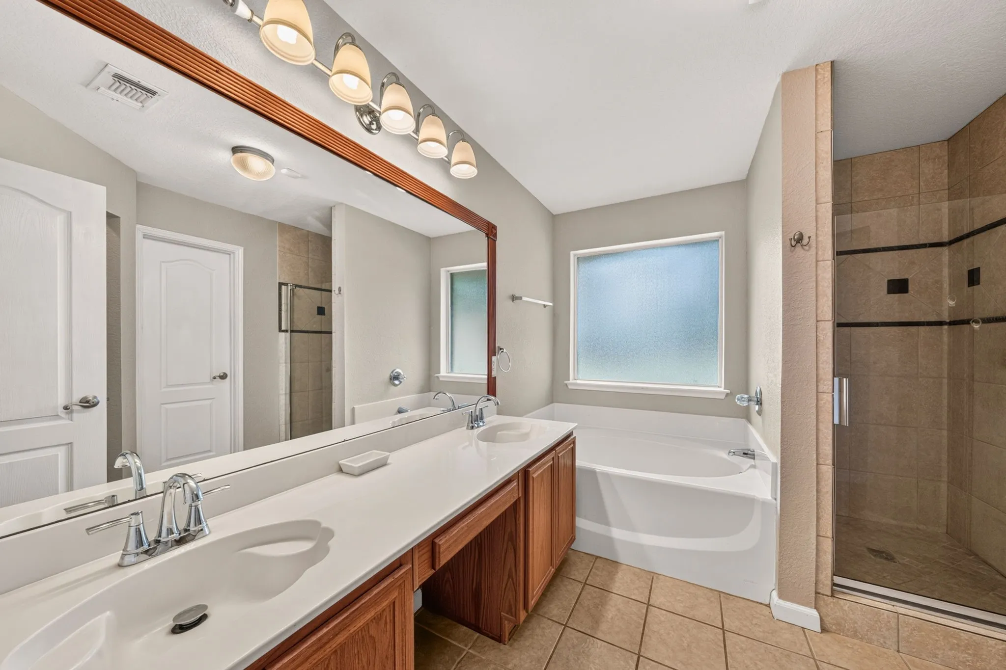 Spa-inspired primary bathroom featuring dual vanities with wood-finish cabinetry, white quartz countertops, and polished chrome faucetry