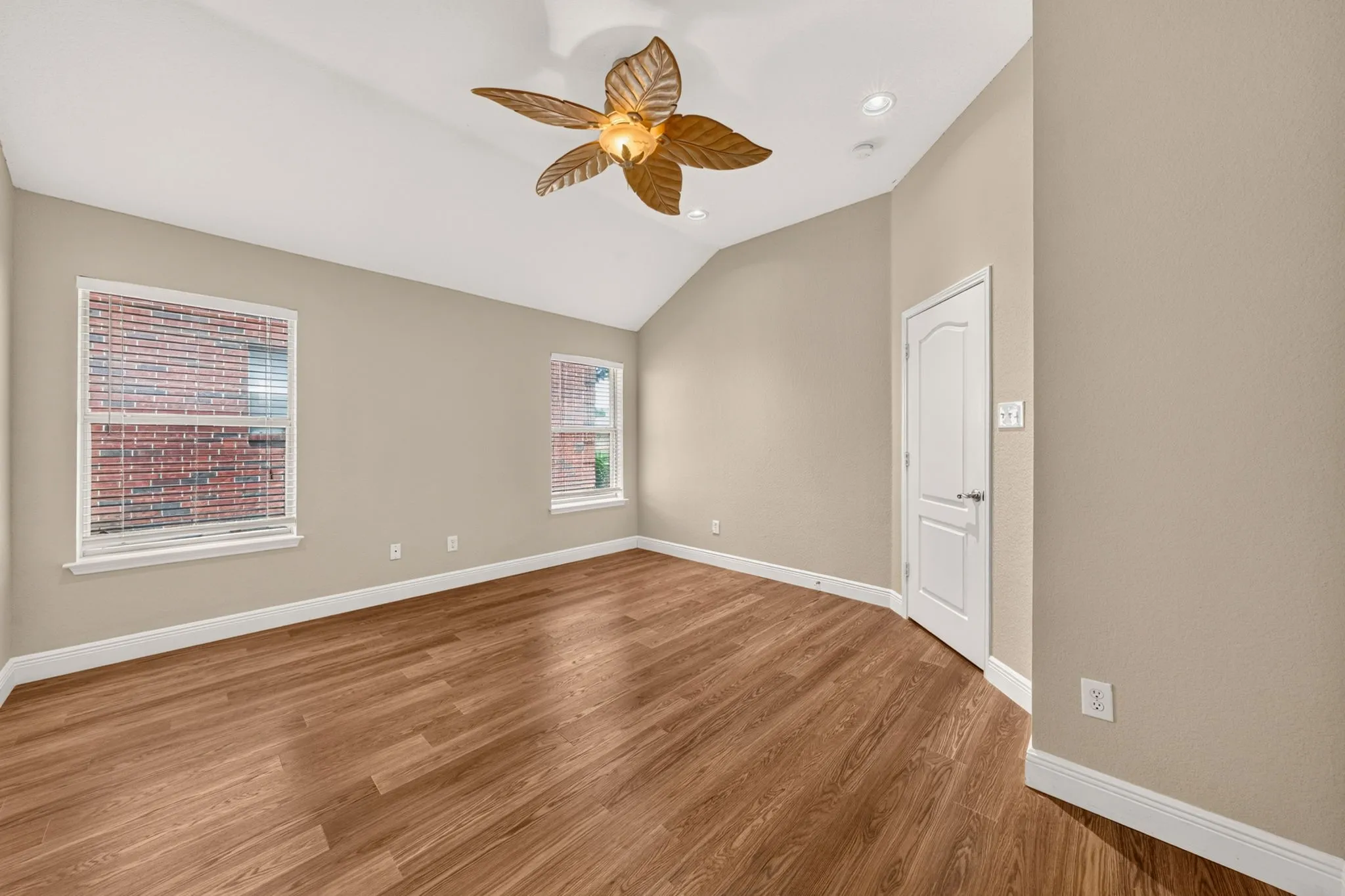 Spacious room showcasing warm wood-finish flooring, neutral taupe walls, and abundant natural light from dual windows