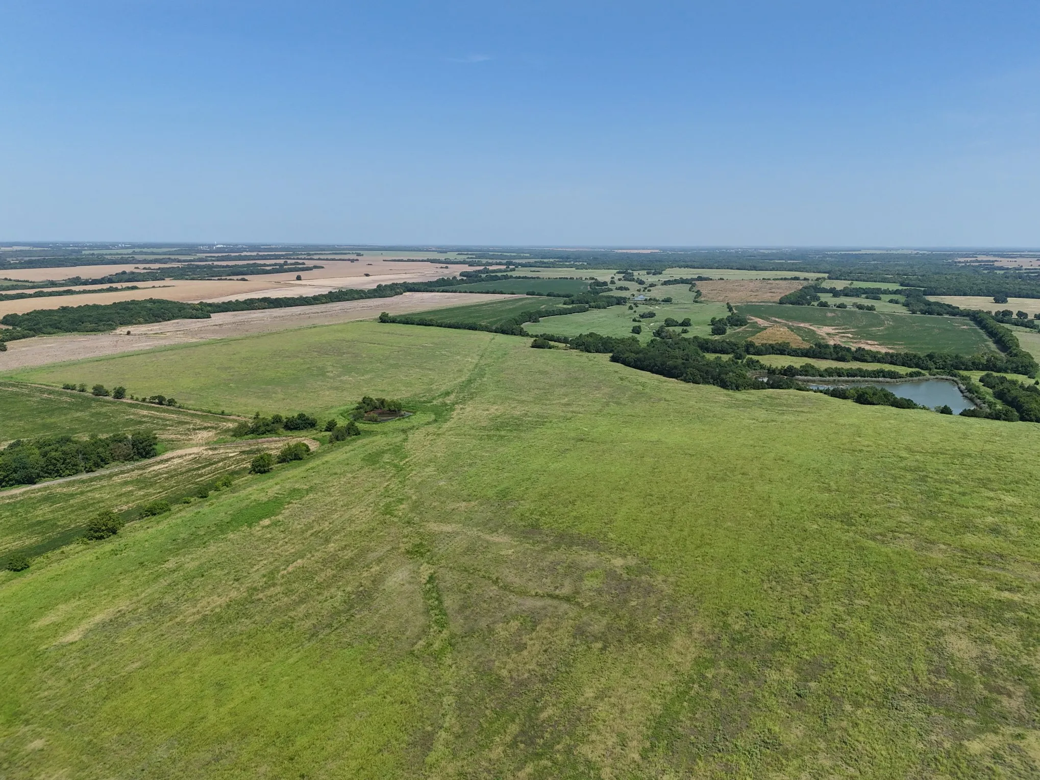 Expansive land showcasing varied terrain, including open fields, wooded areas, and a visible pond