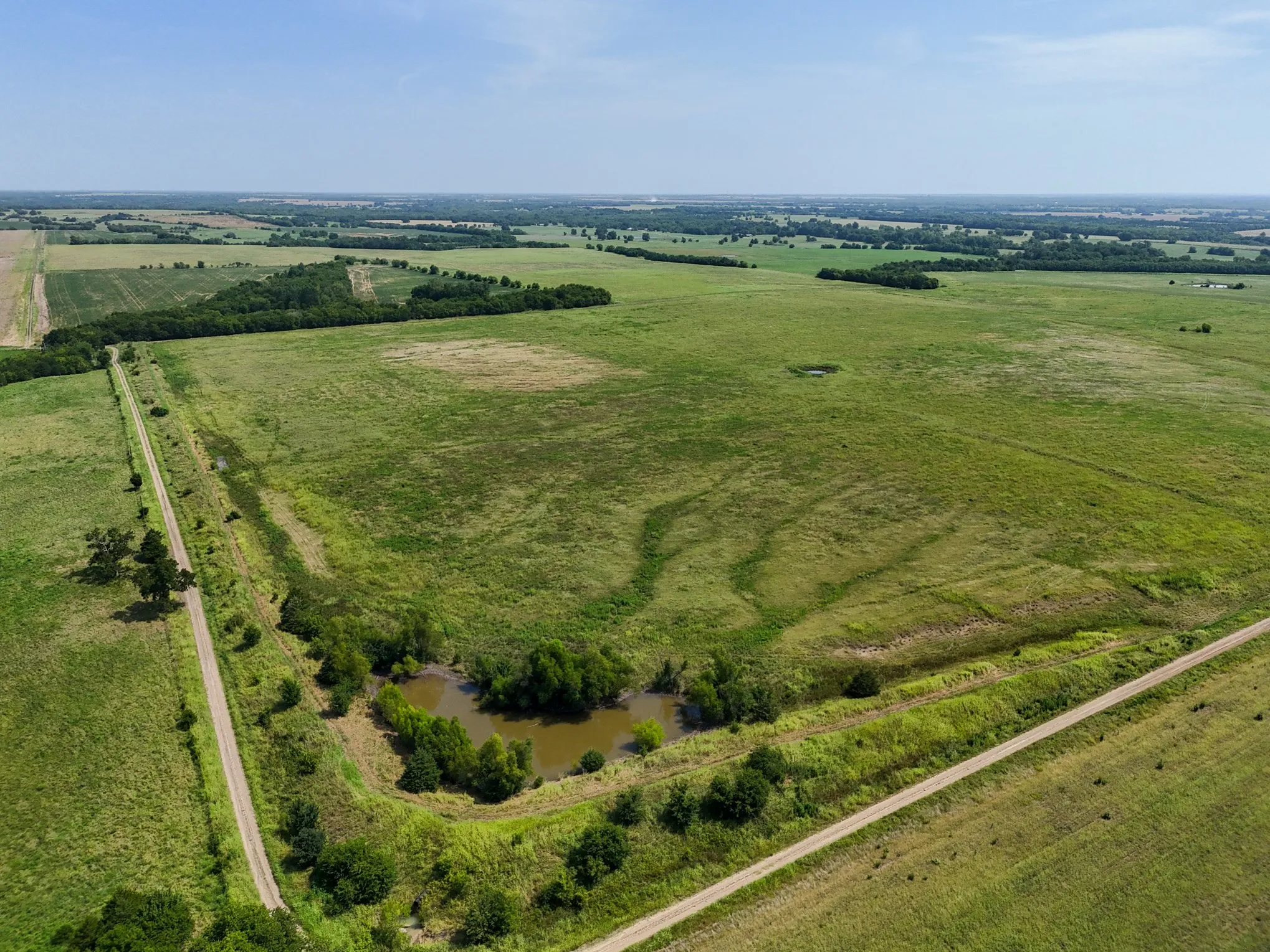 Expansive green landscape featuring a natural pond and bordering wooded areas