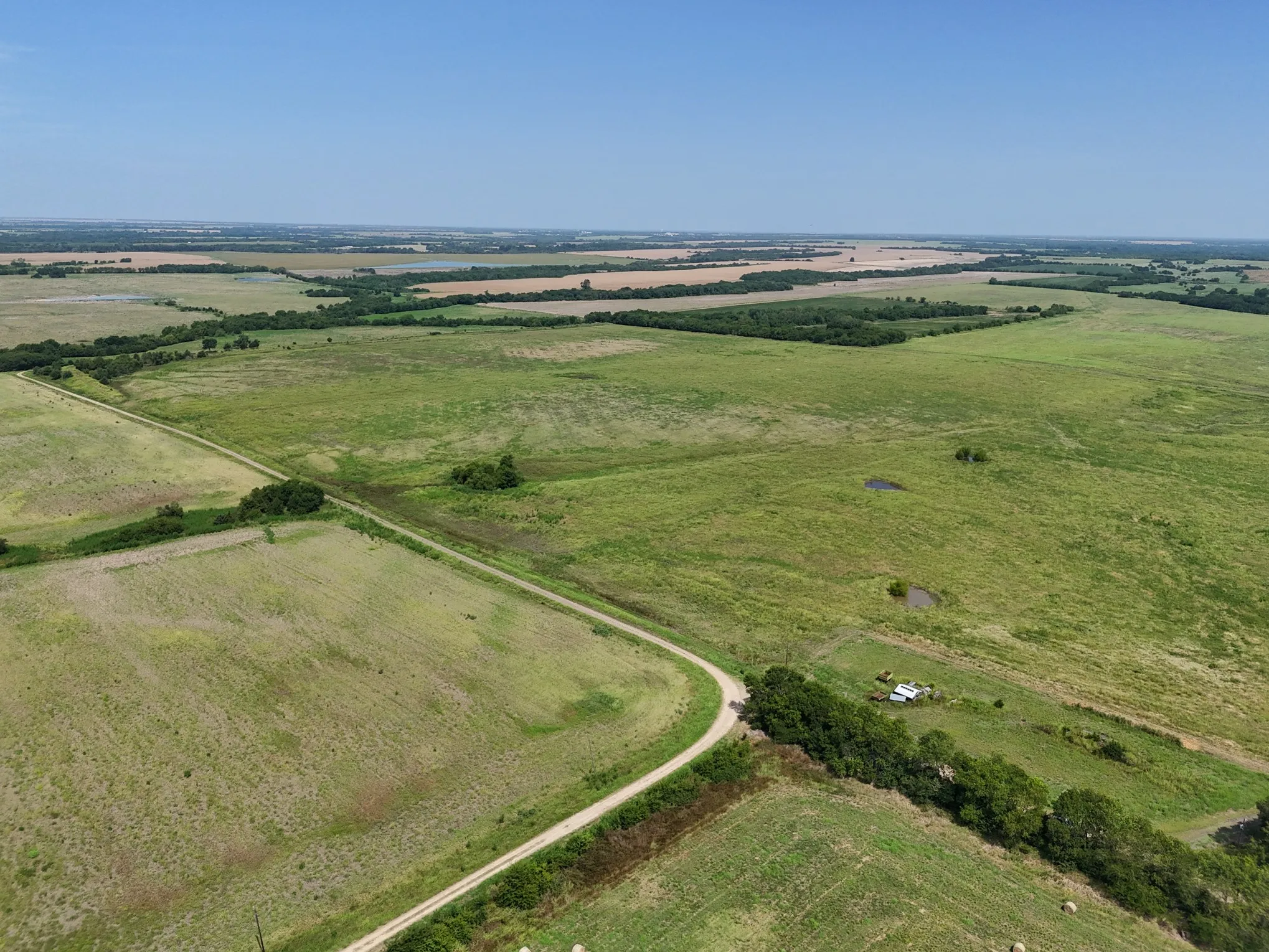 Expansive acreage featuring a winding dirt road, scattered trees, and multiple small ponds
