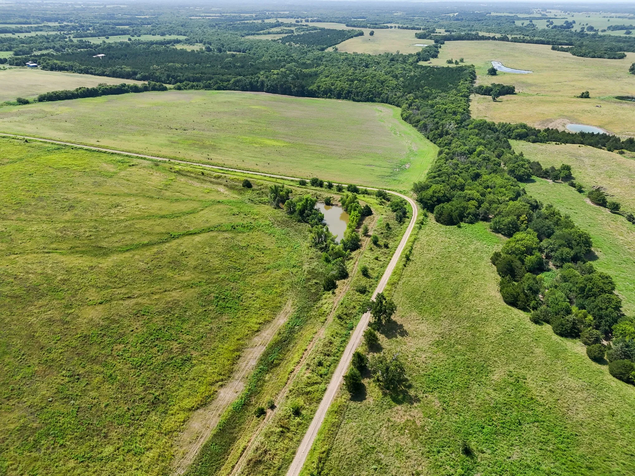 Expansive acreage featuring a winding unpaved road, mature tree lines, and multiple ponds