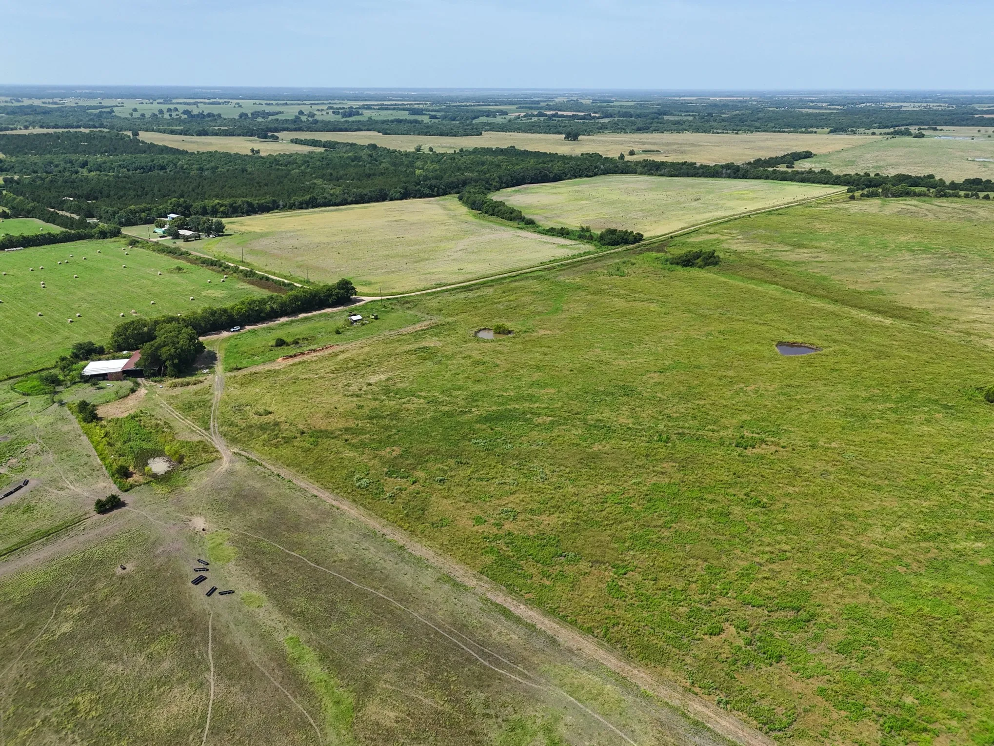 Expansive agricultural land featuring a white-roofed barn, multiple pastures, wooded areas, and two ponds