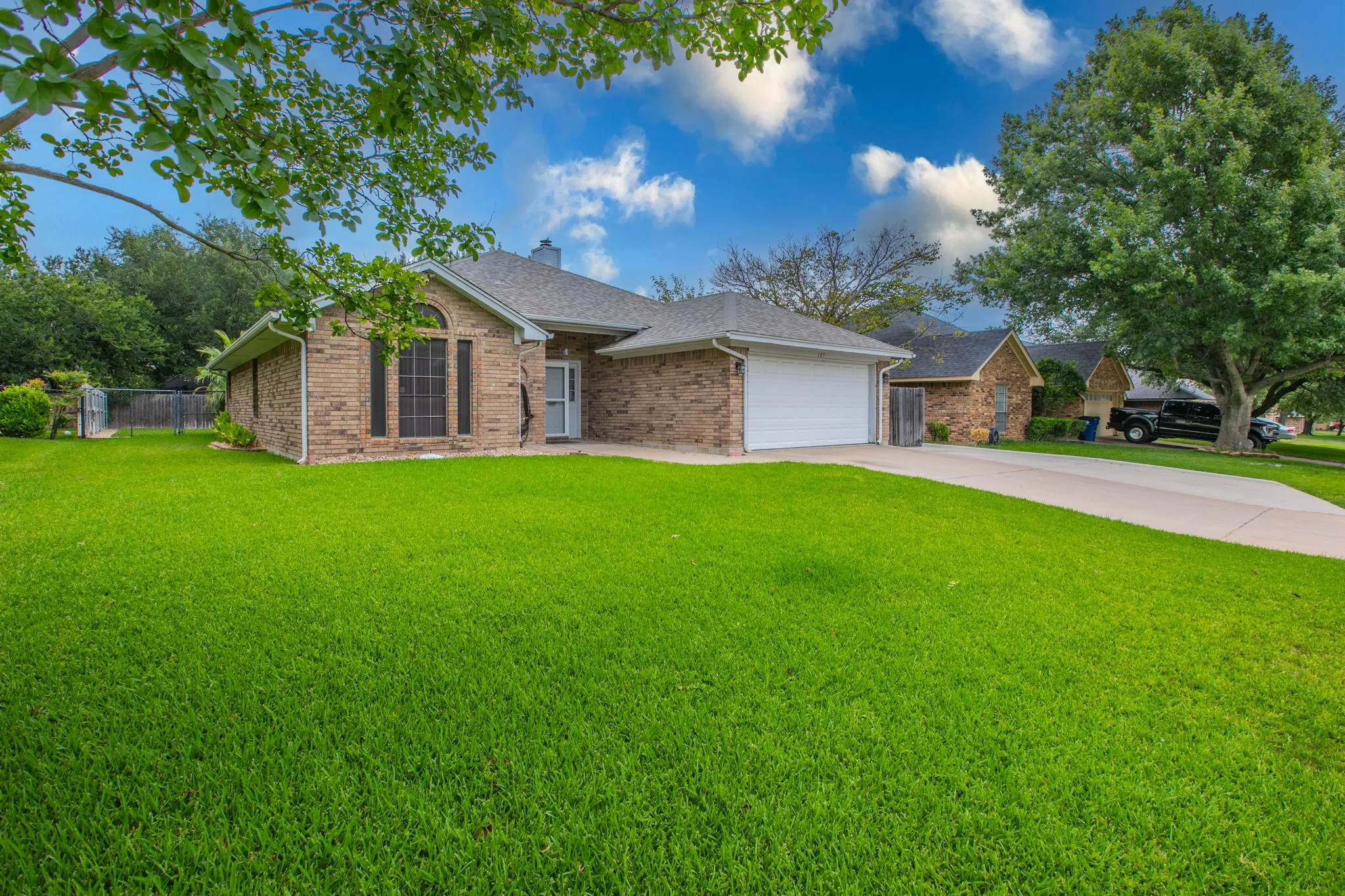 Brick-clad residence featuring an attached garage, a front-facing arched window with shutters, and a prominent driveway