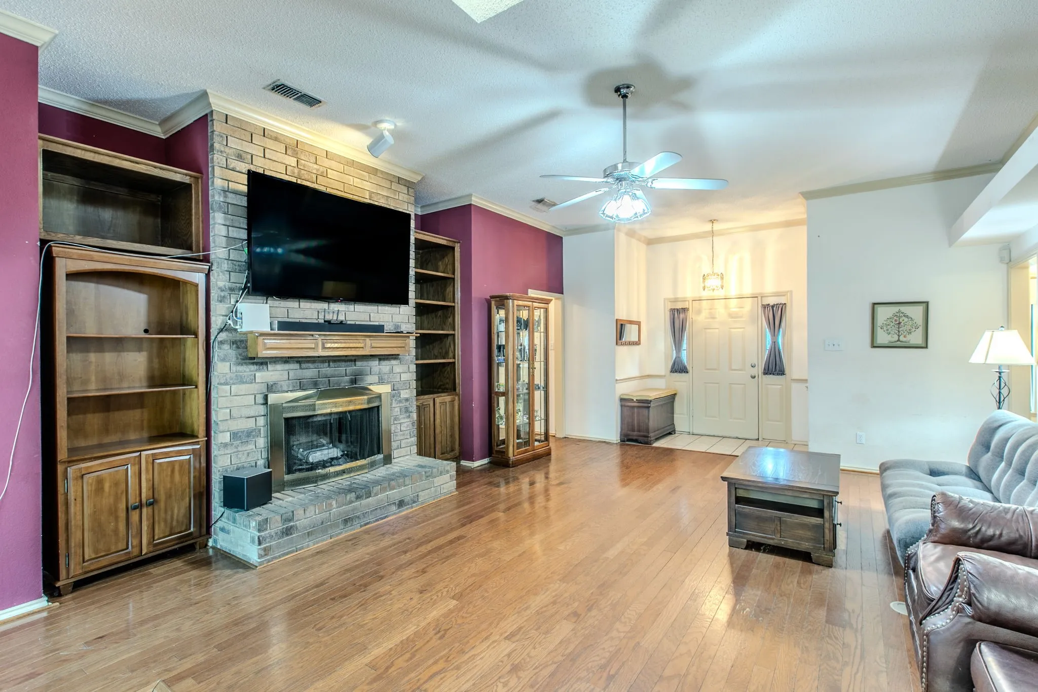 Spacious living area featuring a brick fireplace with a wood mantel, wood-finish flooring, and crown molding