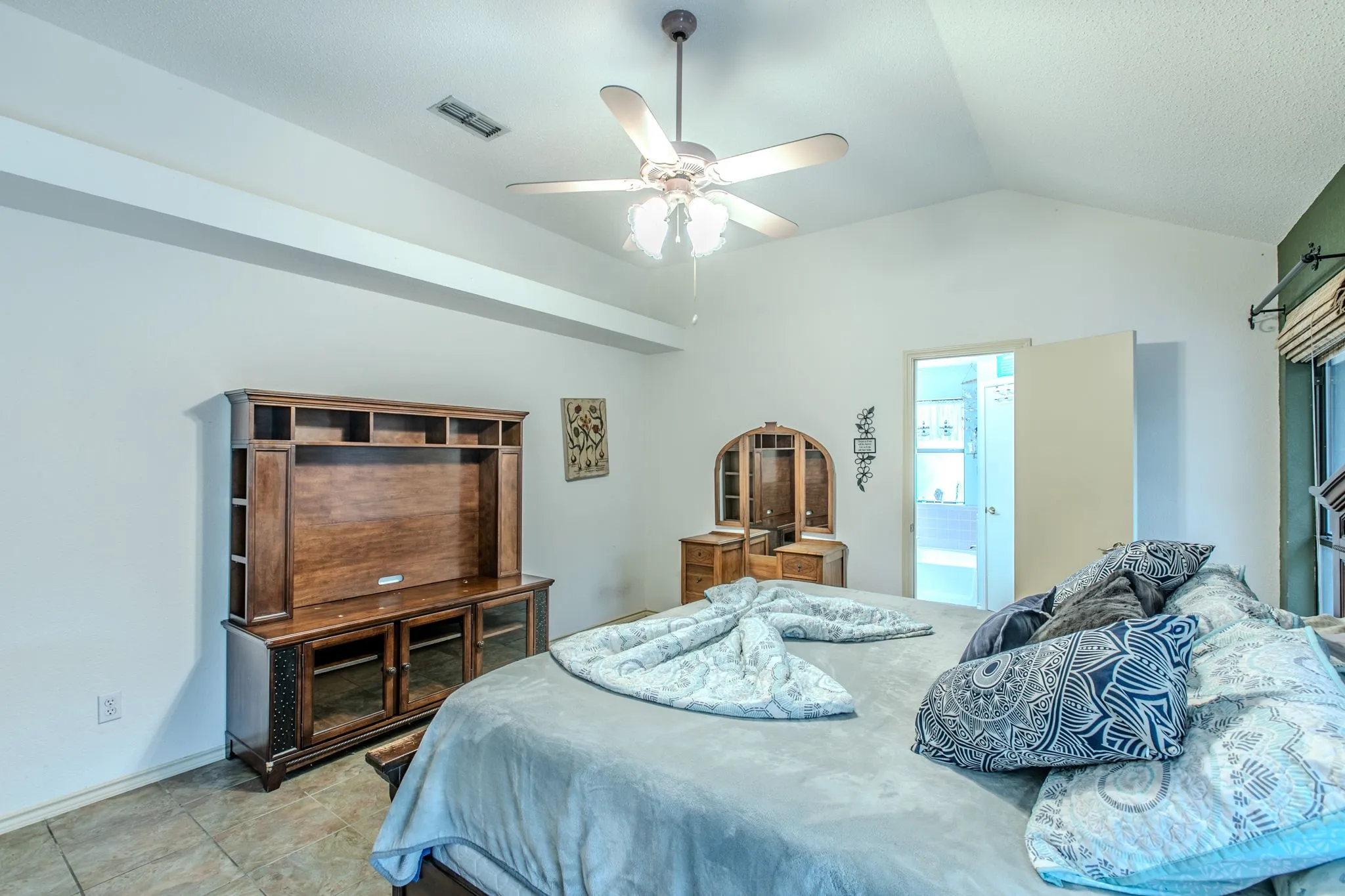 Vaulted ceiling bedroom featuring a ceiling fan, tile flooring, and a doorway opening to an adjacent space