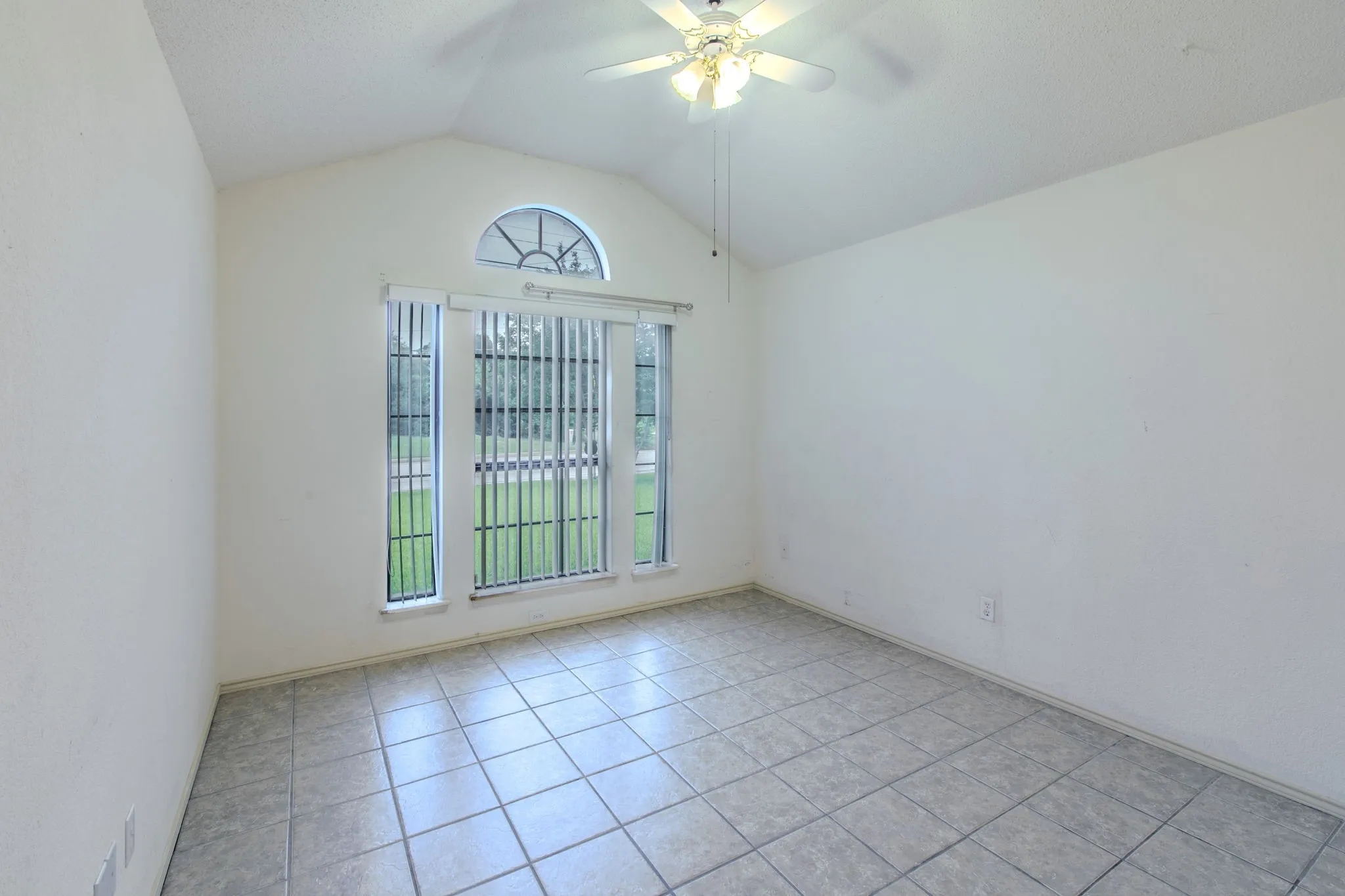 Vaulted ceiling room featuring tiled flooring, a multi-pane window assembly with a half-round transom, and a ceiling fan with integrated lighting