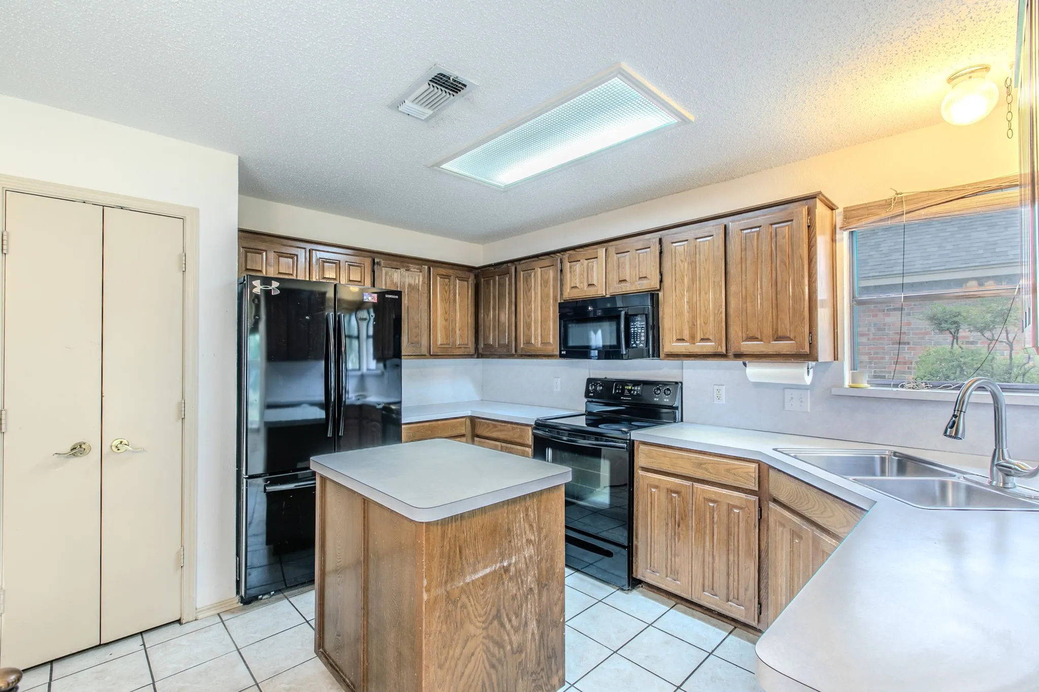 Kitchen featuring wood cabinetry, white countertops, a central island, black appliances, and tile flooring