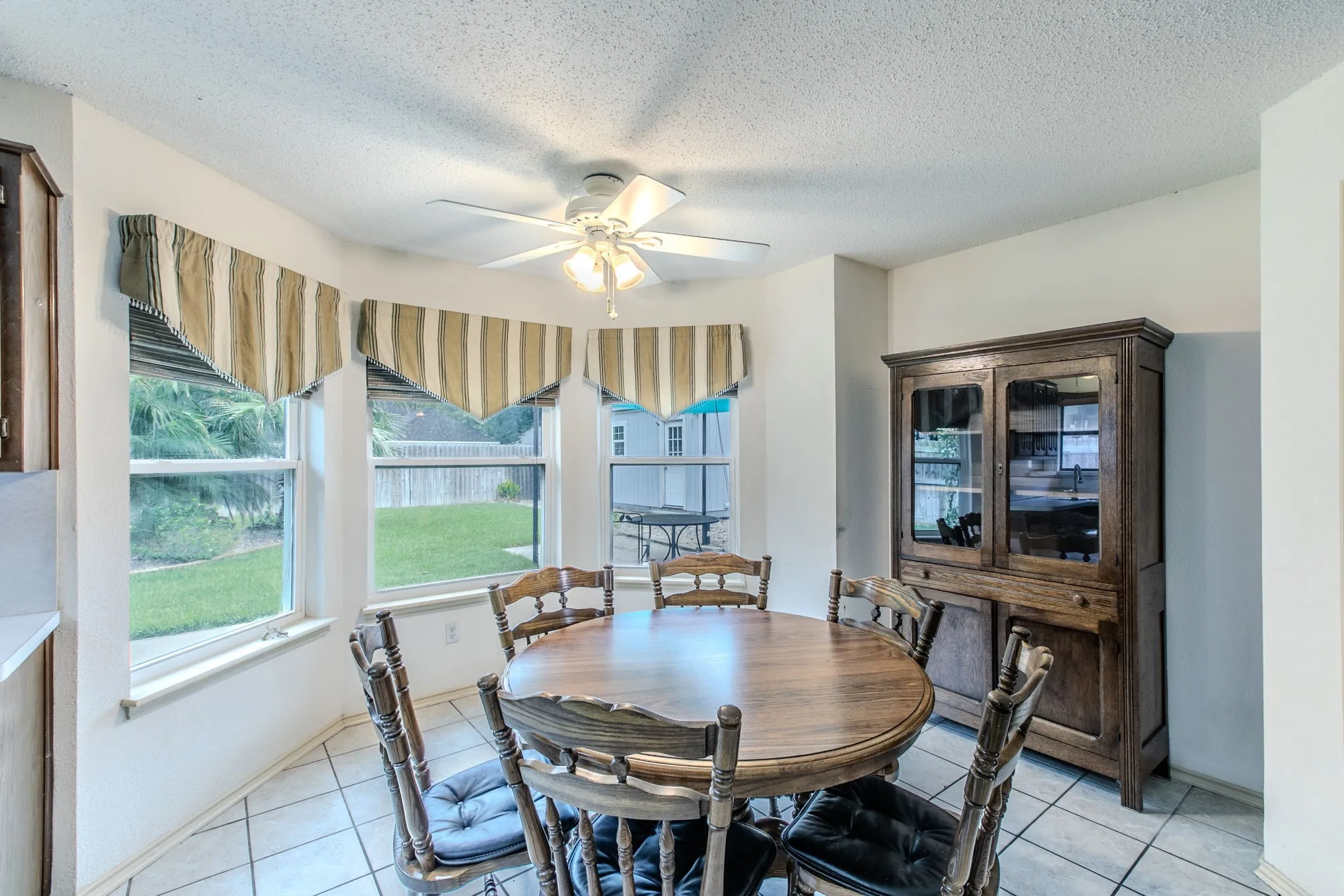 Bay window dining nook featuring tile flooring, a ceiling fan, and access to outdoor green space