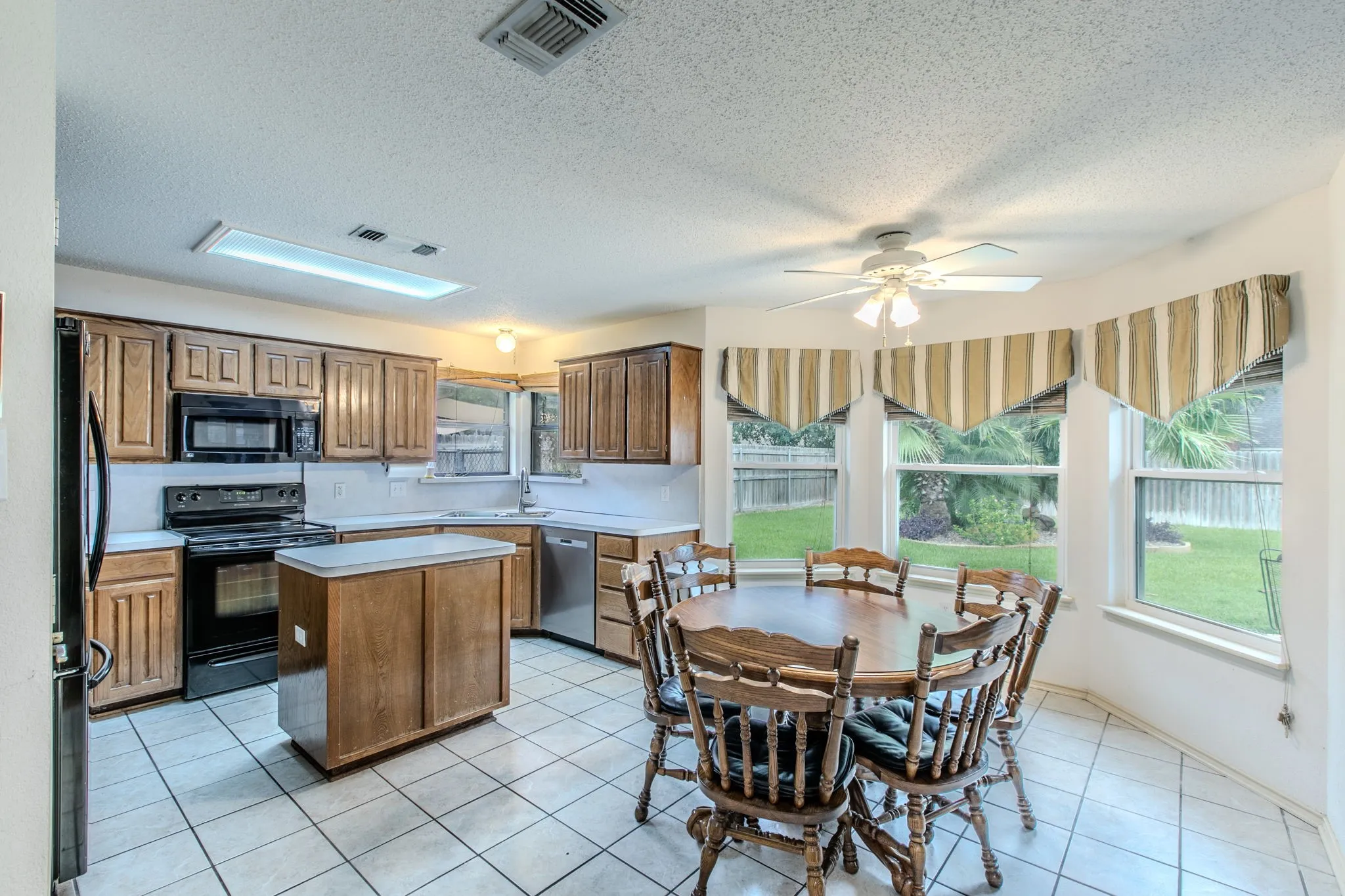 Kitchen with wood-finish cabinetry, black appliances, light countertops, and tile flooring